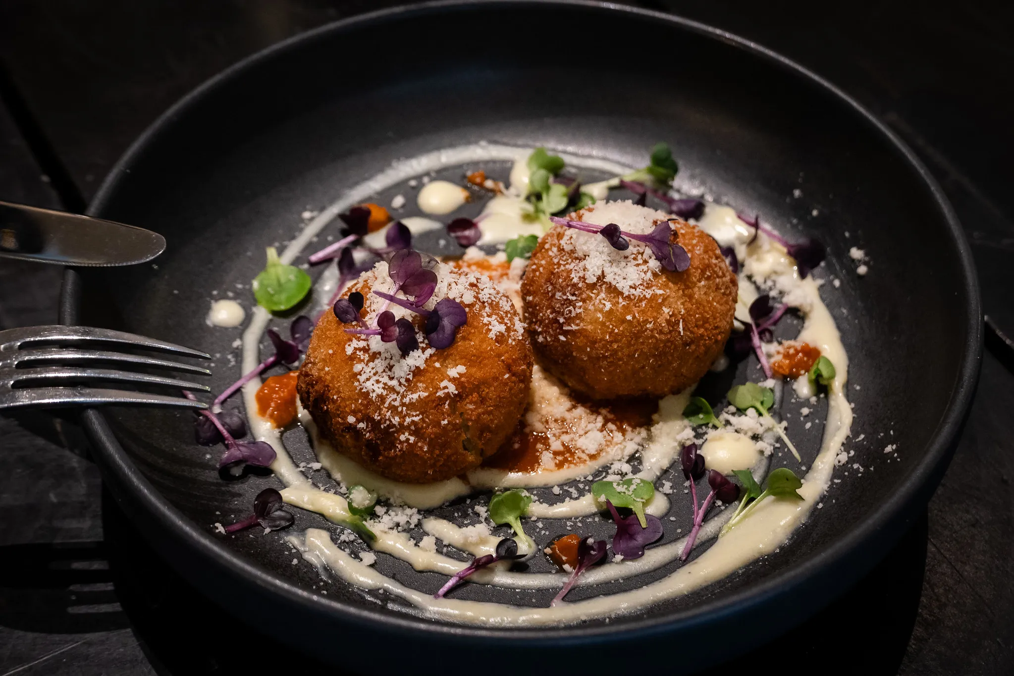 Zwei goldene Arancini auf weißer Creme mit Microgreens, Gastronomie-Fotografie.