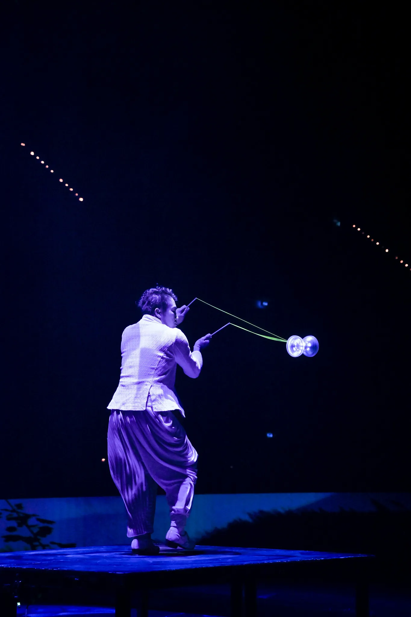 Zirkusartist mit Diabolo in blauem Bühnenlicht, schwebende Bewegung festgehalten in der Kulturfotografie.