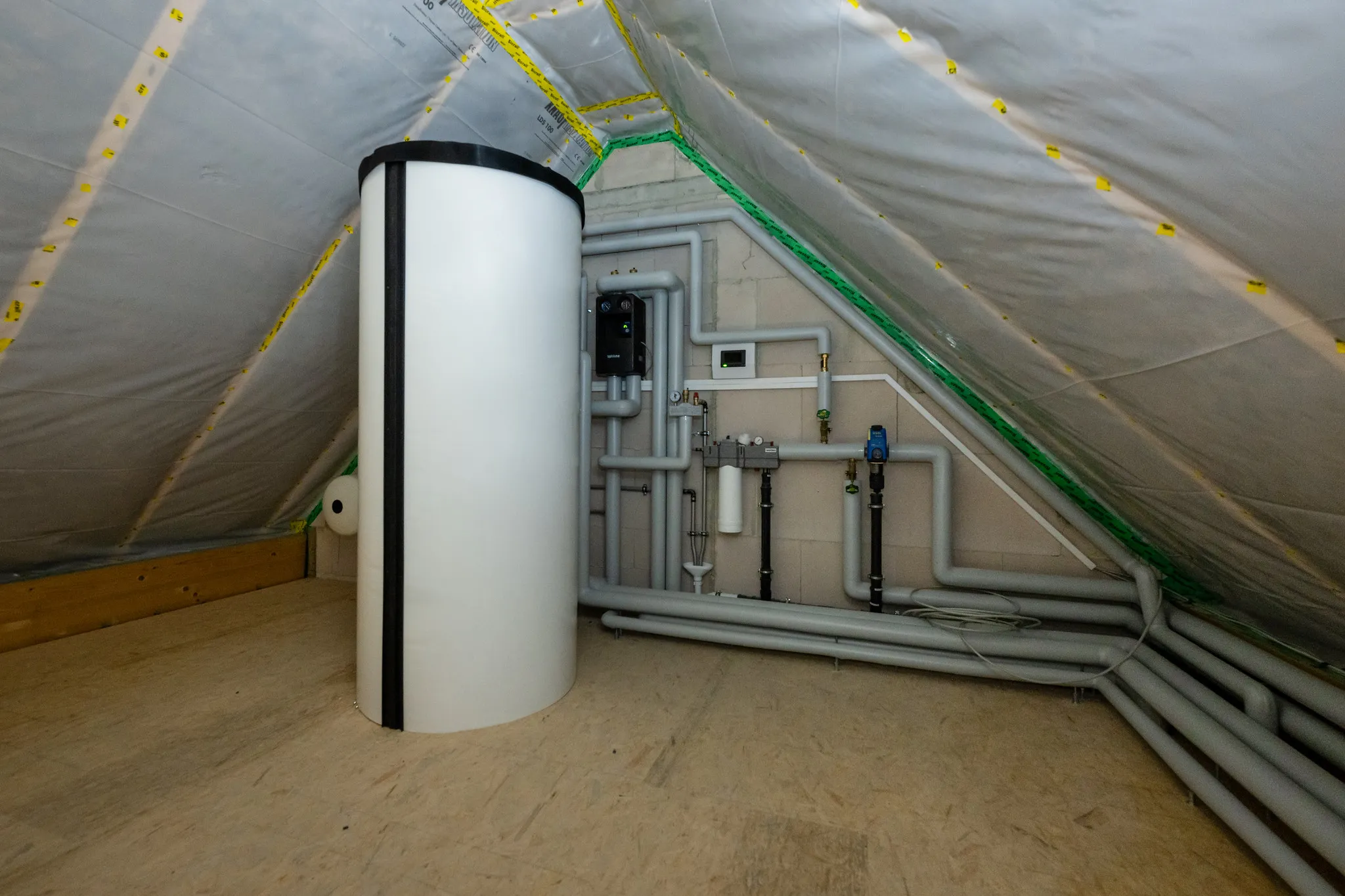 Dachgeschoss-Technikraum mit Pufferspeicher und Heizungsrohren.