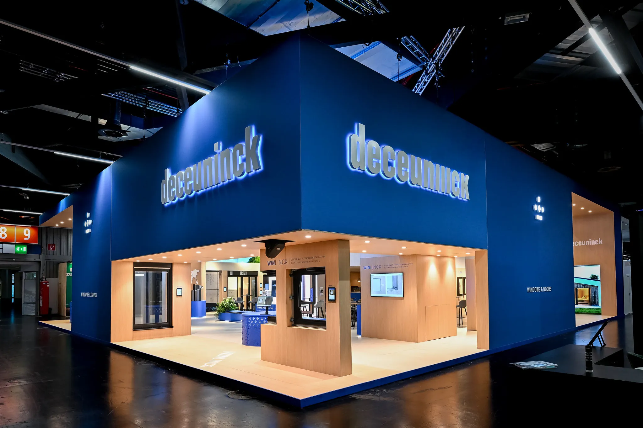 Imposante Außenansicht des blauen Deceuninck-Messestands als leuchtender Würfel in der Messehalle Nürnberg.