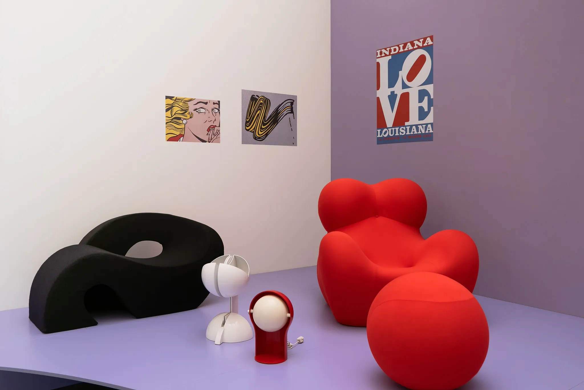 Design-Möbel Inszenierung mit rotem Bubble-Chair, schwarzem Sofa und Retro-Lampen vor Pop-Art-Postern.