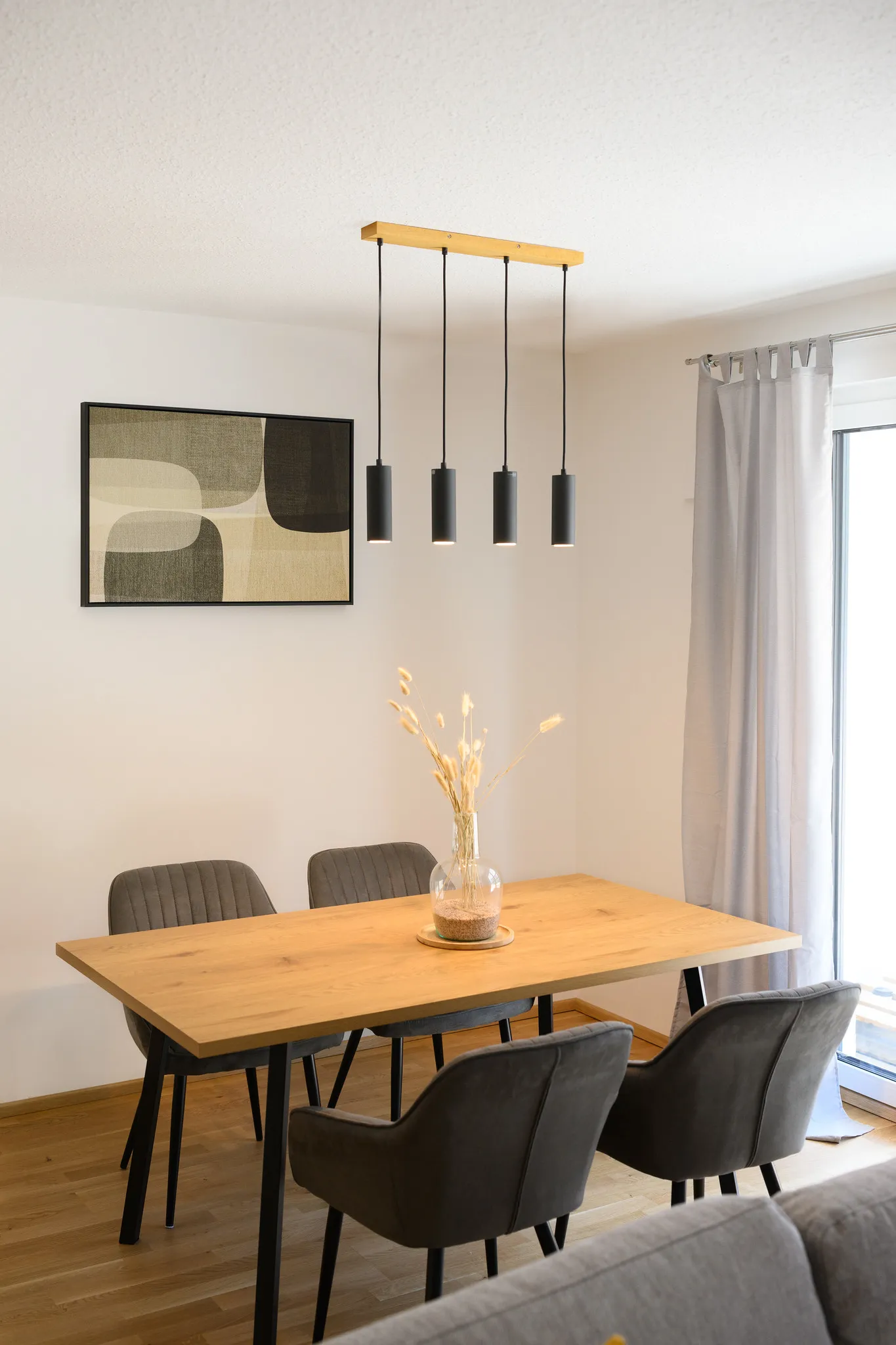 Esszimmer mit Holztisch, Pendelleuchten und Wandbild.