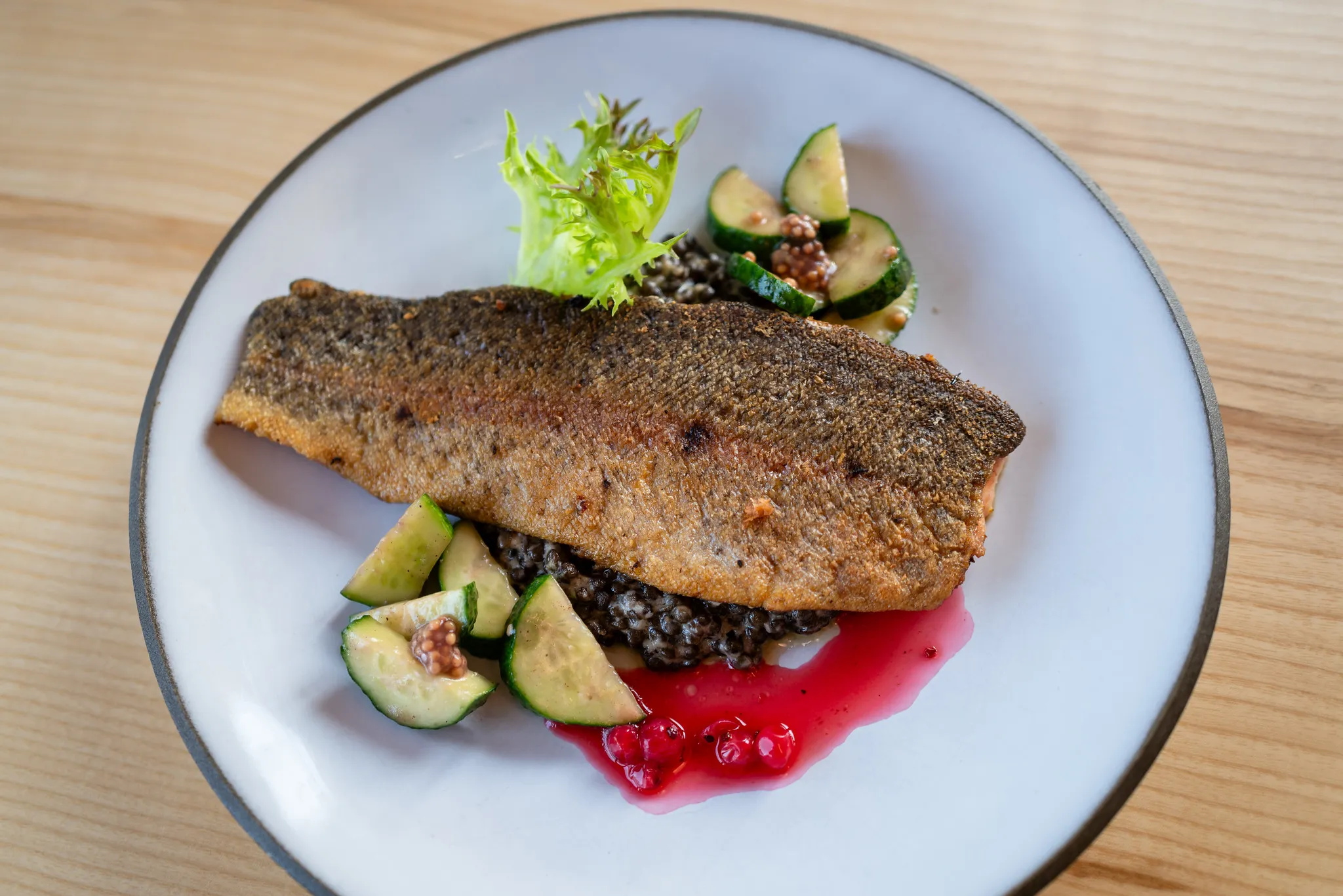 Knuspriges Forellenfilet auf schwarzen Linsen mit Preiselbeeren, Food-Fotografie.
