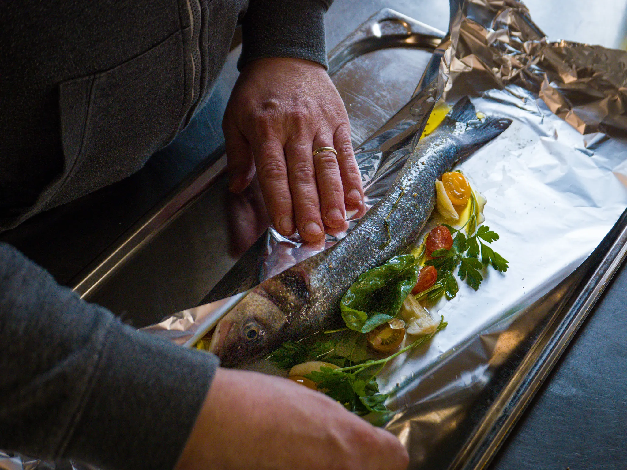 Ganzer Fisch auf Alufolie mit Tomaten, Zitrone und Kräutern, Küchenfotografie.