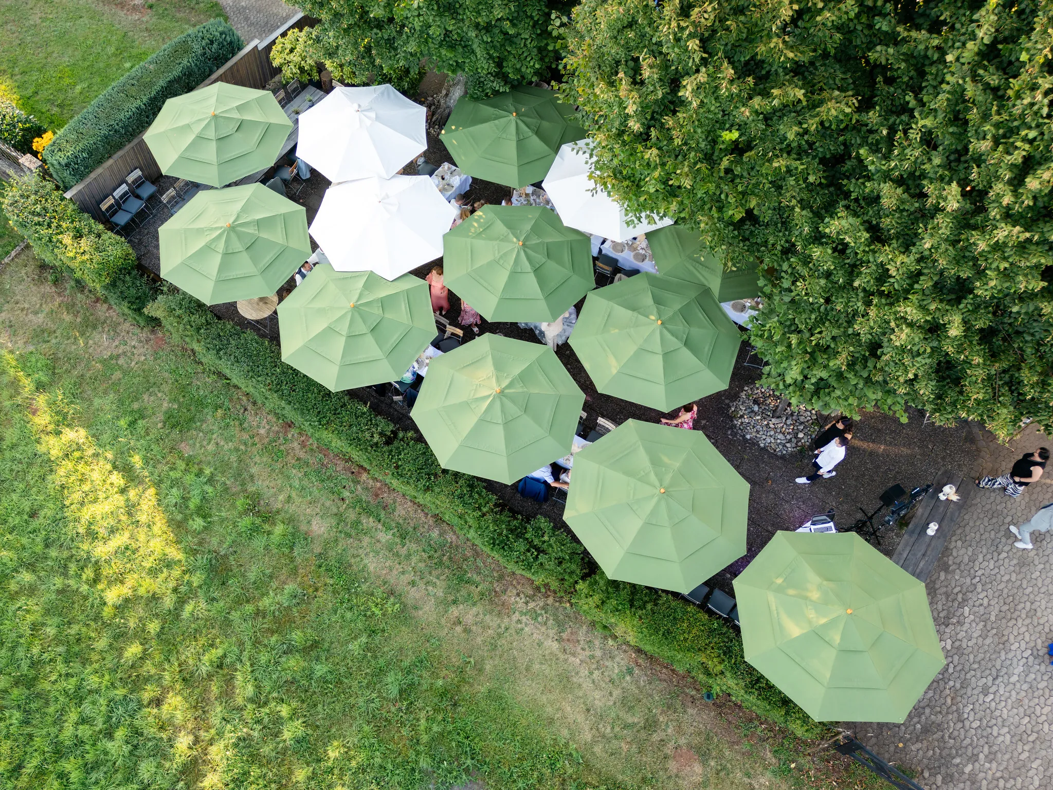 Drohnenaufnahme einer Gartenterrasse mit grünen und weißen Sonnenschirmen von oben
