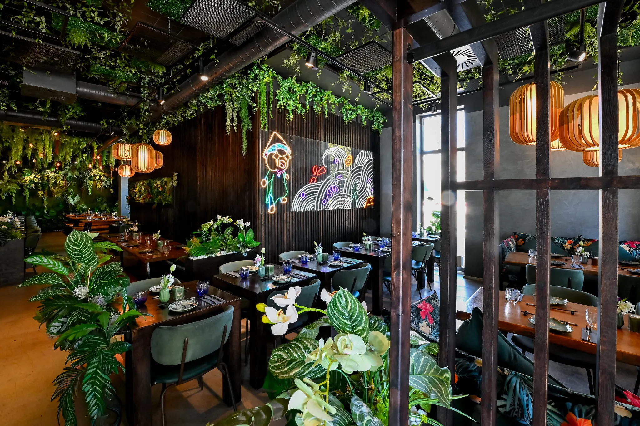 Gastraum mit üppiger Dschungelbegrünung, Lampions und Neon-Kunstwerk, Restaurantfotografie Nürnberg.