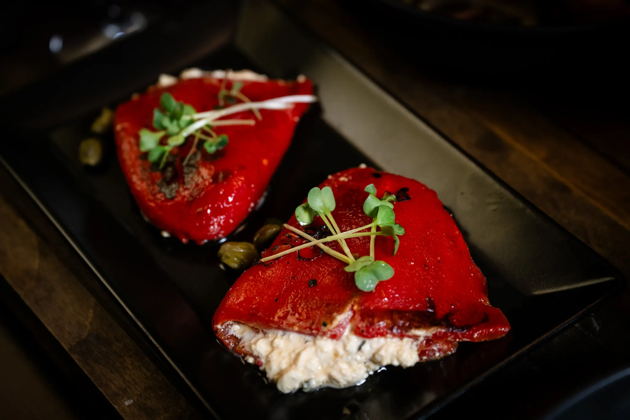 Gefüllte rote Paprika mit Feta und Kapern auf schwarzem Teller, mediterrane Küche.