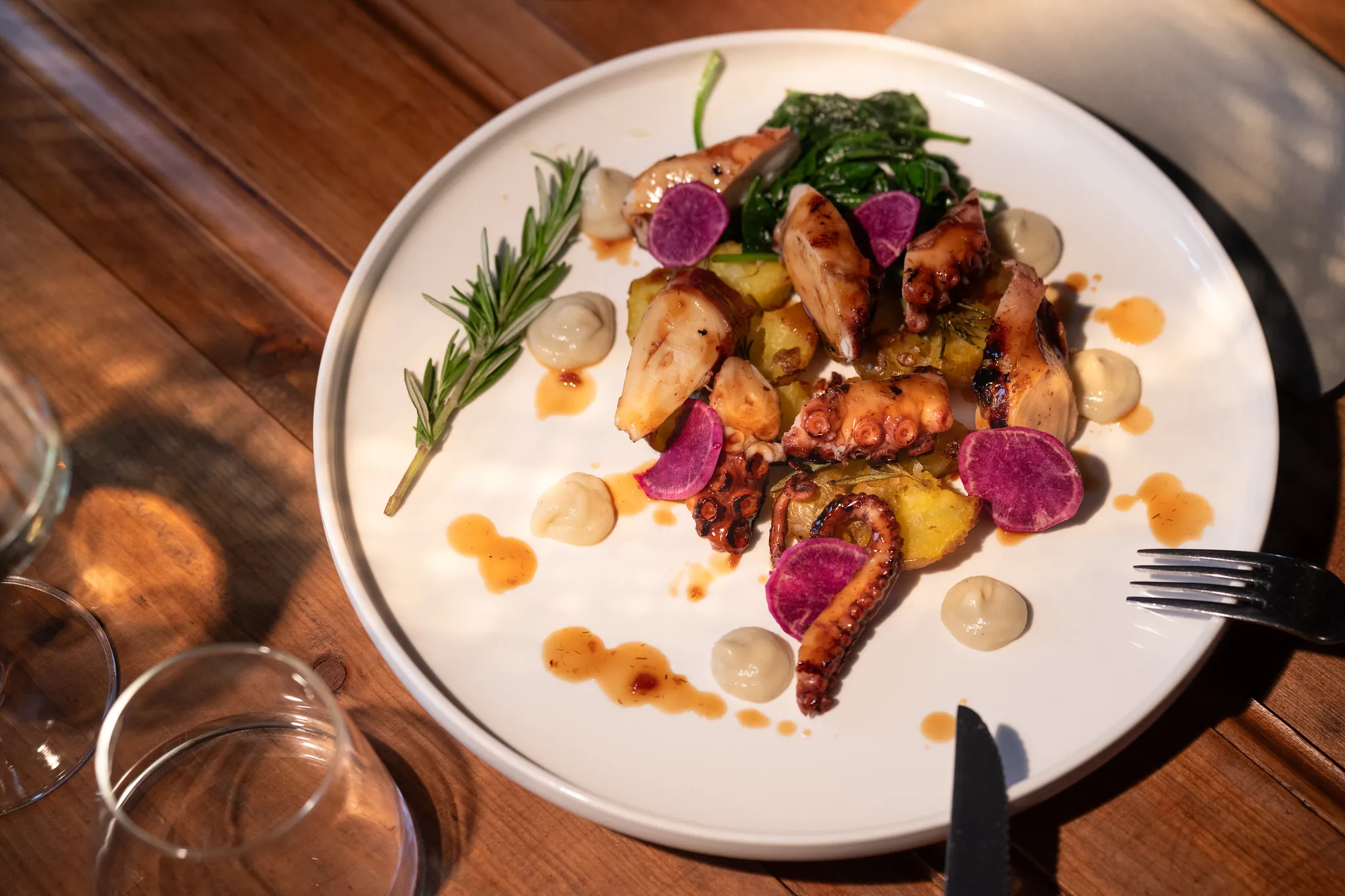 Gegrillter Oktopus mit Kartoffeln, Spinat und lila Radieschen, mediterrane Food-Fotografie.
