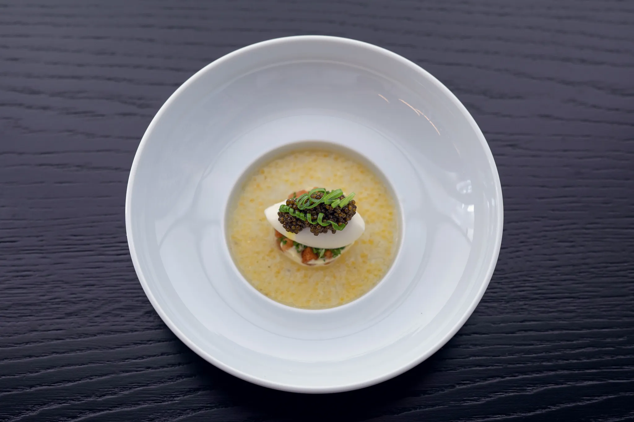 Gourmet-Suppe mit Kaviar-Nocke im tiefen Teller auf dunklem Holztisch, Fine-Dining-Fotografie Nürnberg.