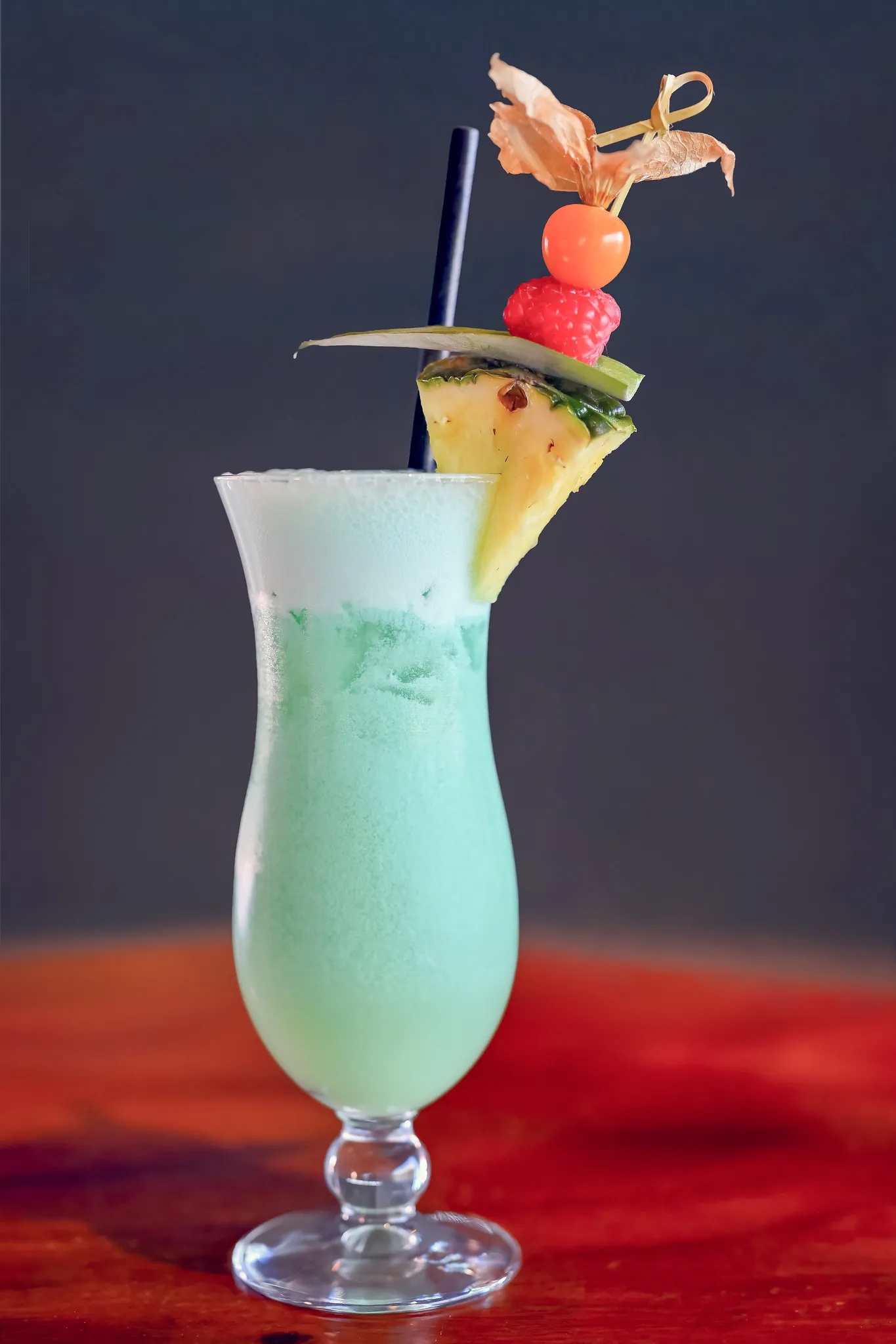 Türkisfarbener Cocktail mit Ananas und Früchten im Hurricane-Glas, Getränke-Fotografie.