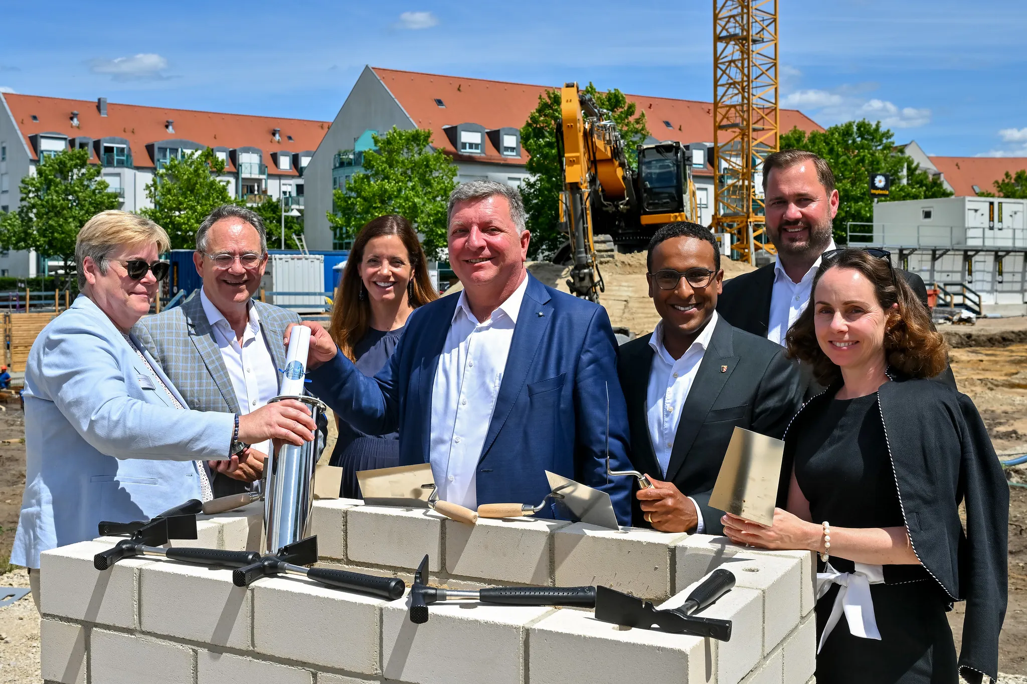 Gruppe mit Kellen und Zeitkapsel bei feierlicher Grundsteinlegung