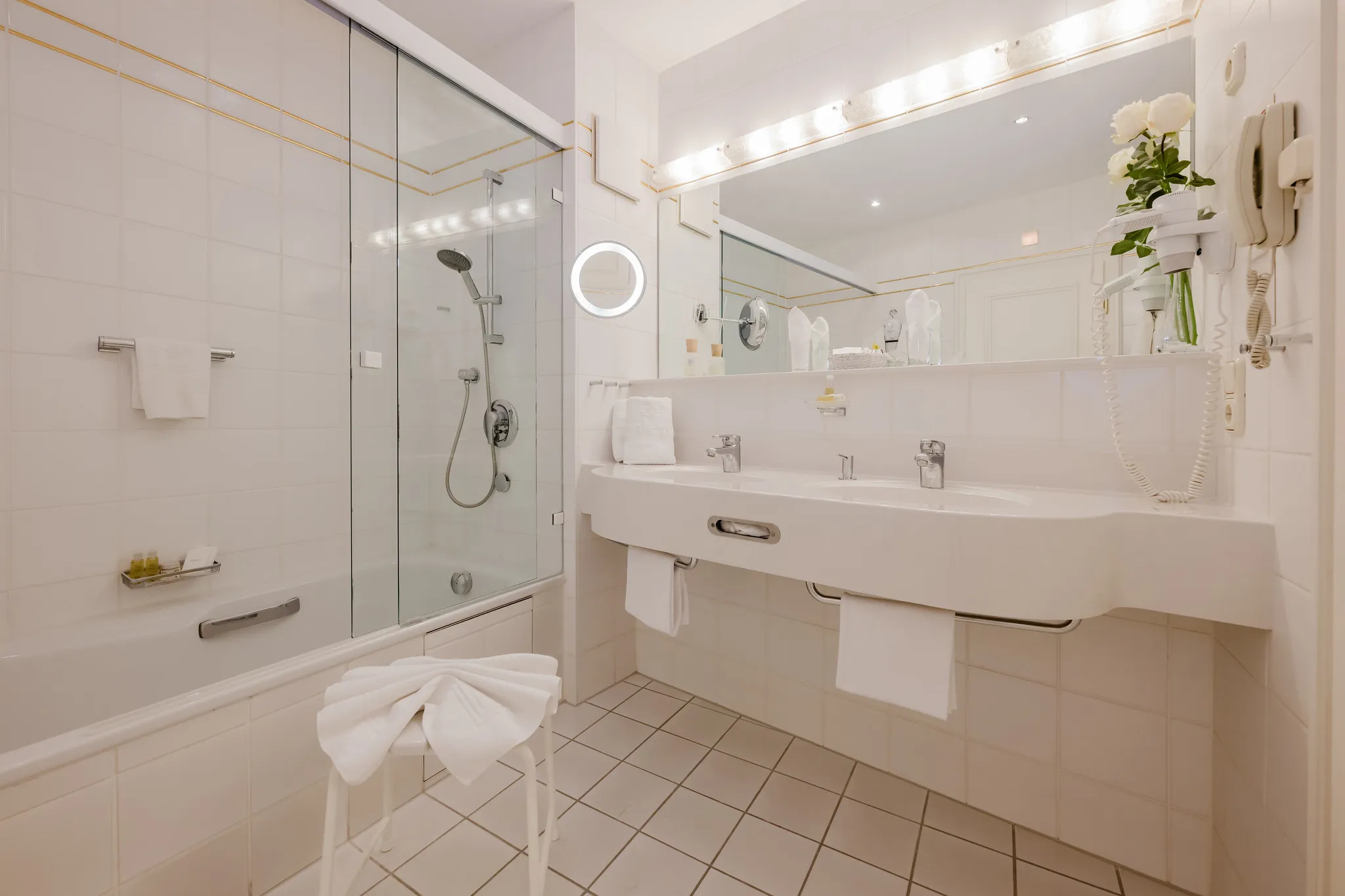 Klassisches Hotelbadezimmer mit großer Badewanne, Doppelwaschtisch und beleuchtetem Spiegel