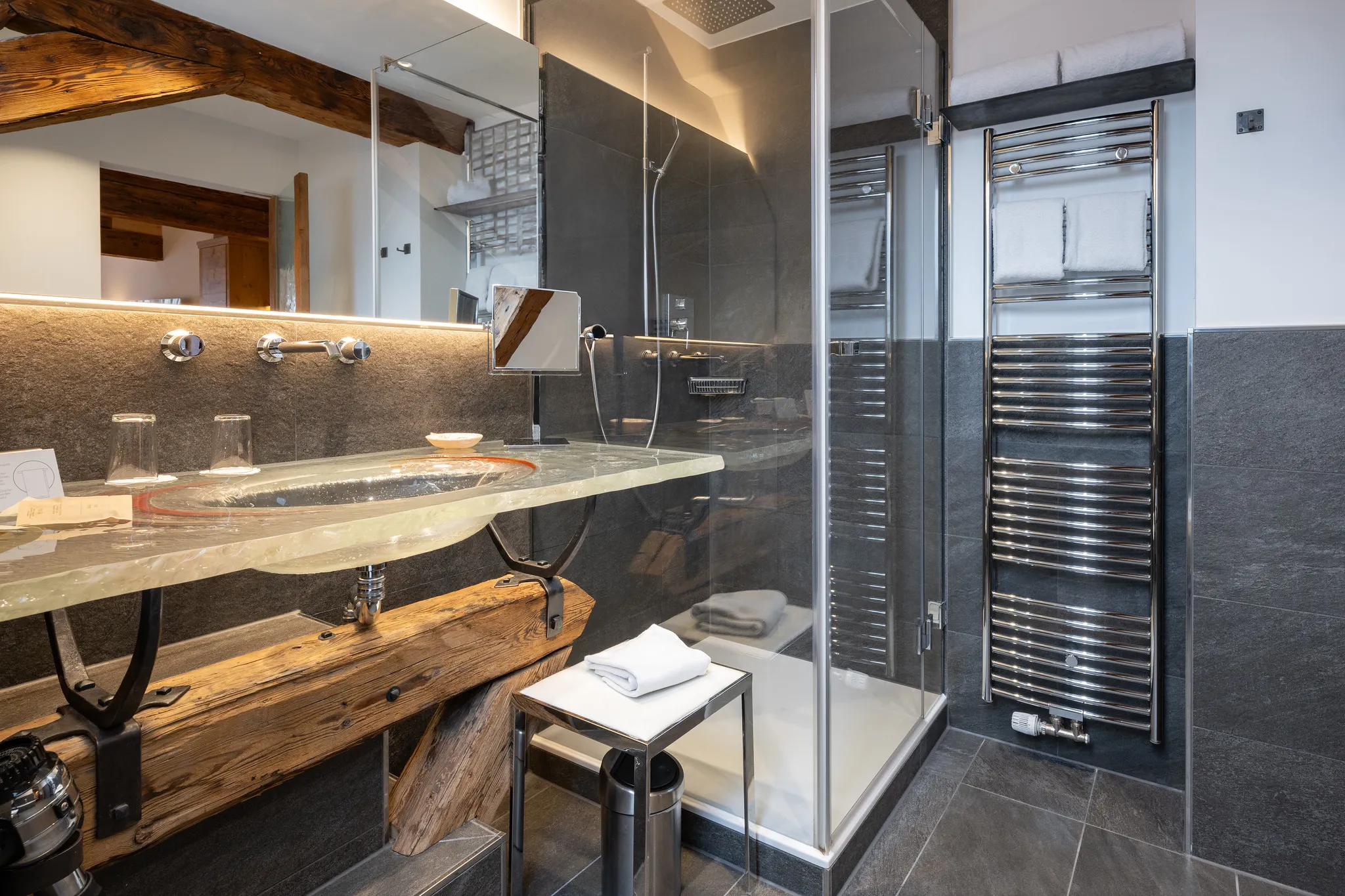 Hotelbadezimmer mit Naturstein-Waschbecken, Holzelementen und moderner Glasdusche