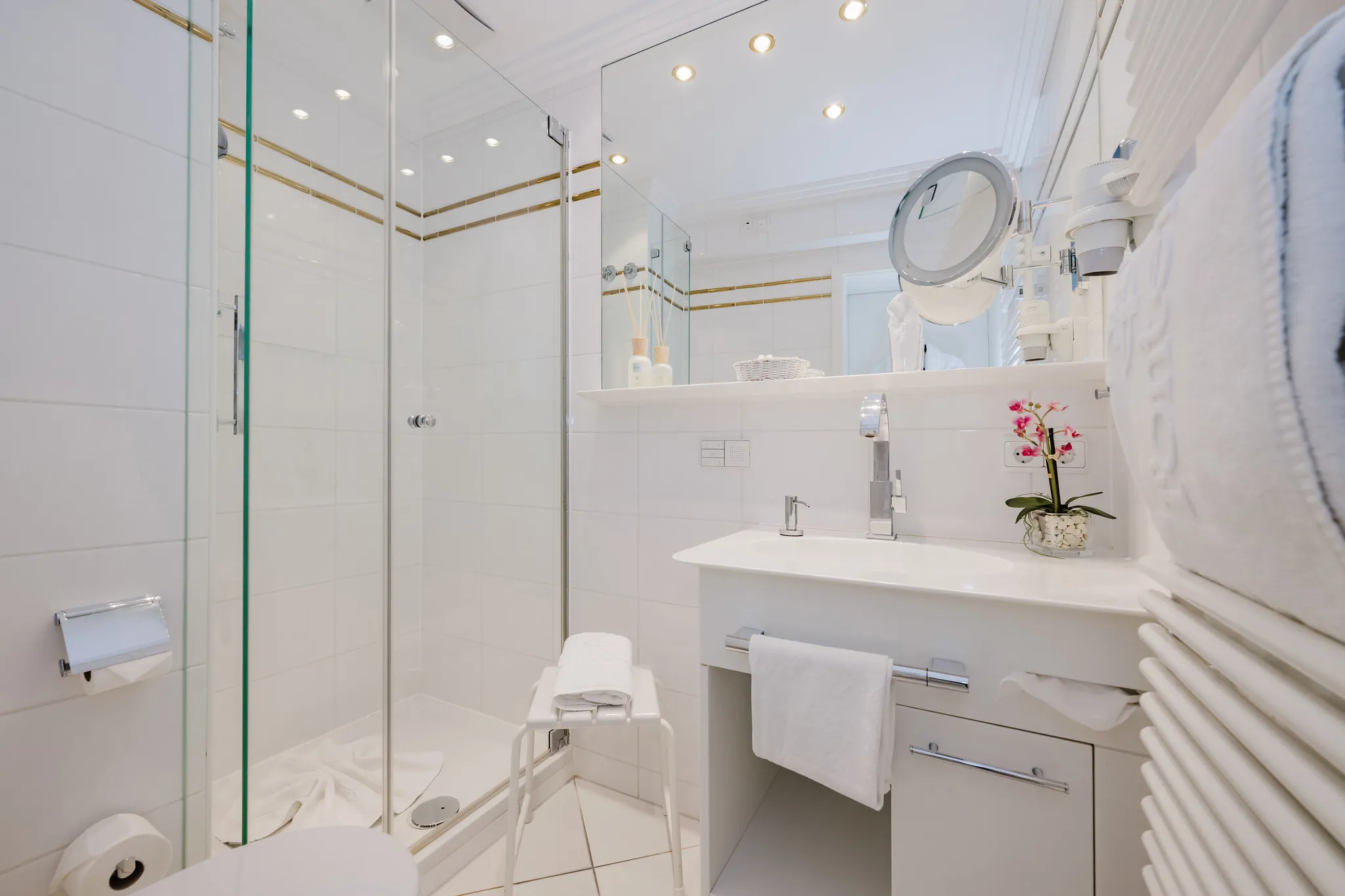 Helles Hotelbadezimmer in Weiß mit Orchidee-Dekoration, Dusche und Handtuchheizung