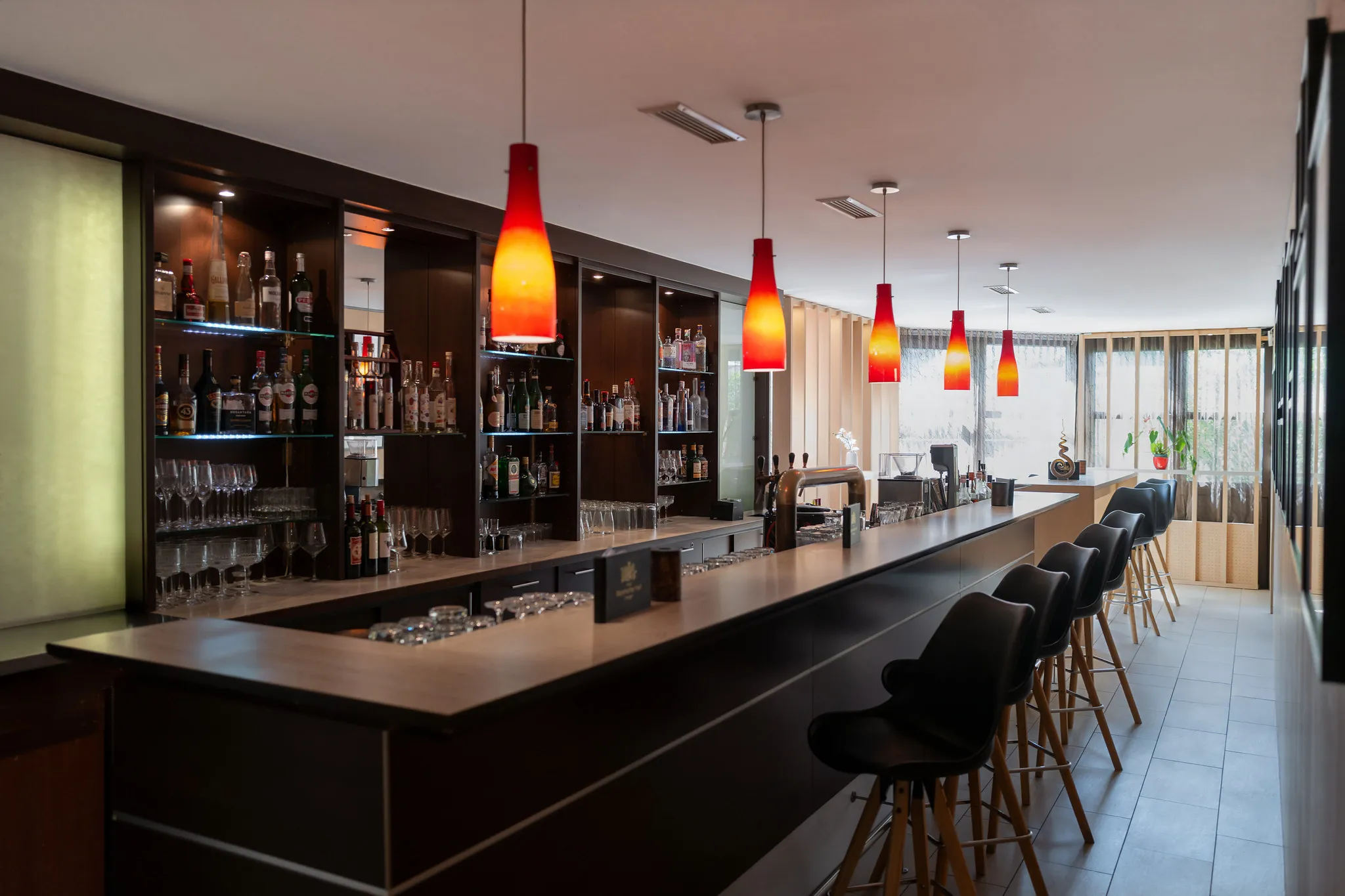 Elegante Hotelbar mit roten Hängelampen, gut bestückter Flaschenwand und schwarzen Barhockern