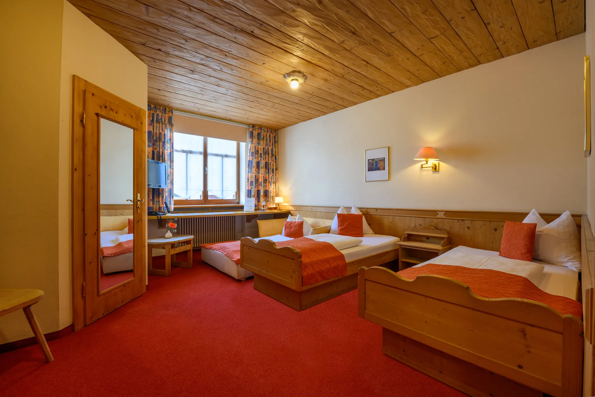 Traditionelles Hotel-Doppelzimmer mit Holzbetten, rotem Teppich und gemütlichem Landhausstil
