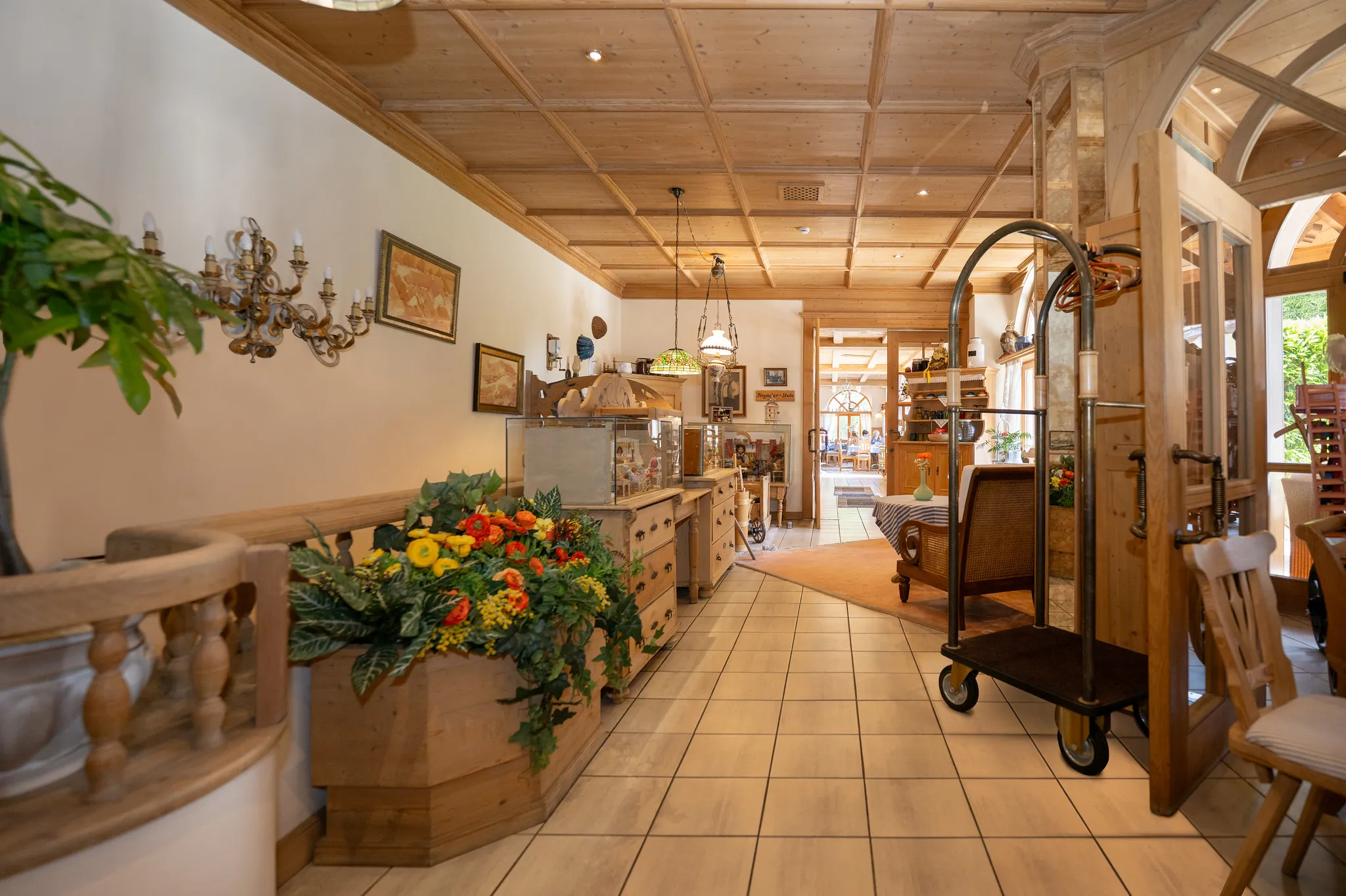 Gemütliches Hotel-Foyer mit Holzdecke, frischem Blumenarrangement und Gepäckwagen am Empfang