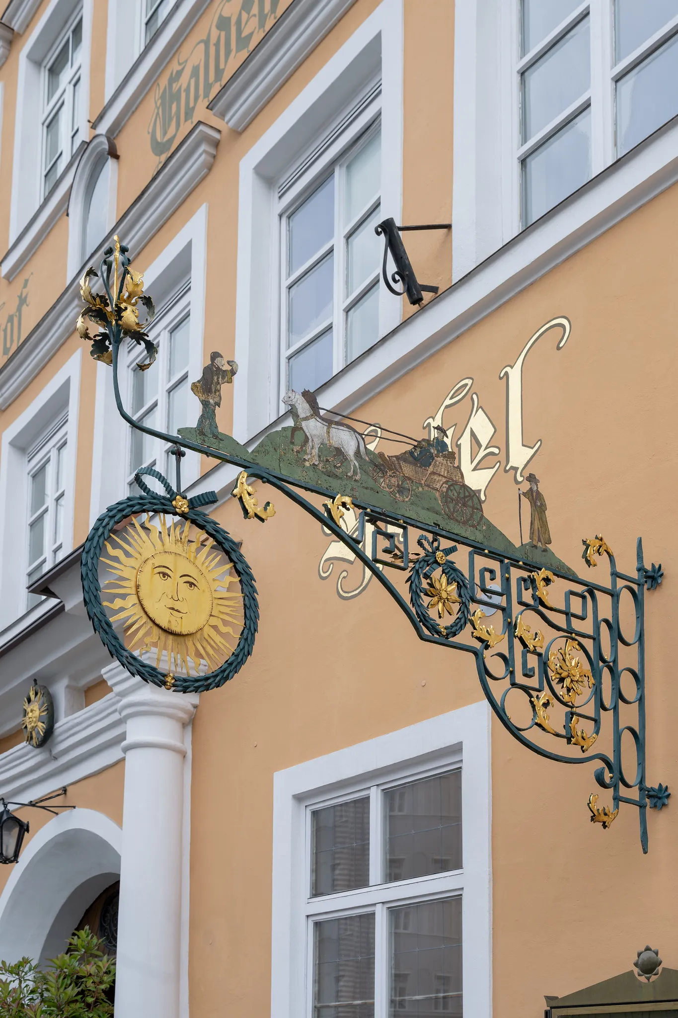Kunstvolles schmiedeeisernes Schild des Hotels Goldene Sonne mit Sonnen-Motiv an der Fassade