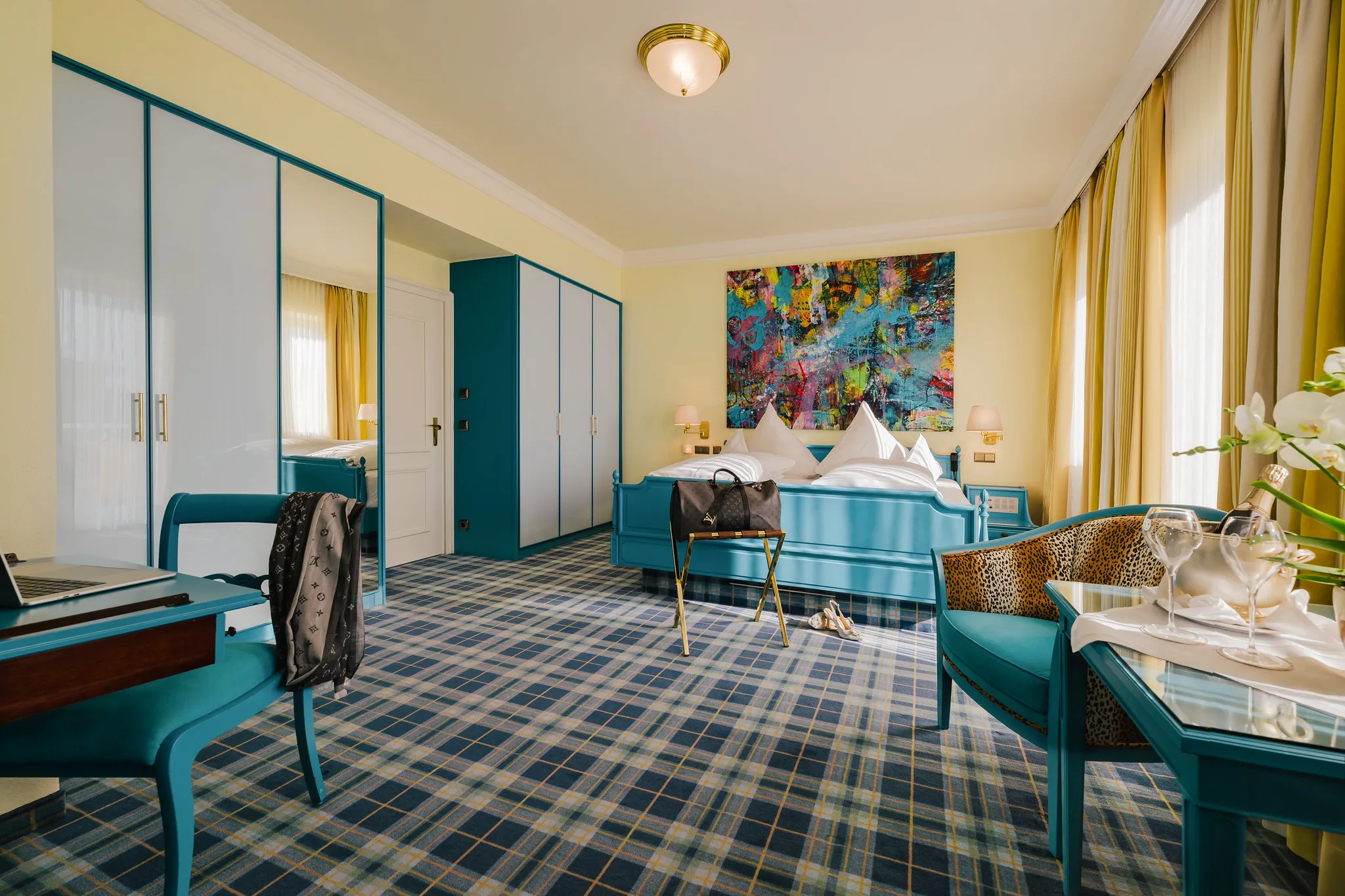 Extravagante Hotel-Suite mit blauen Möbeln, abstraktem Wandbild und kariertem Teppich