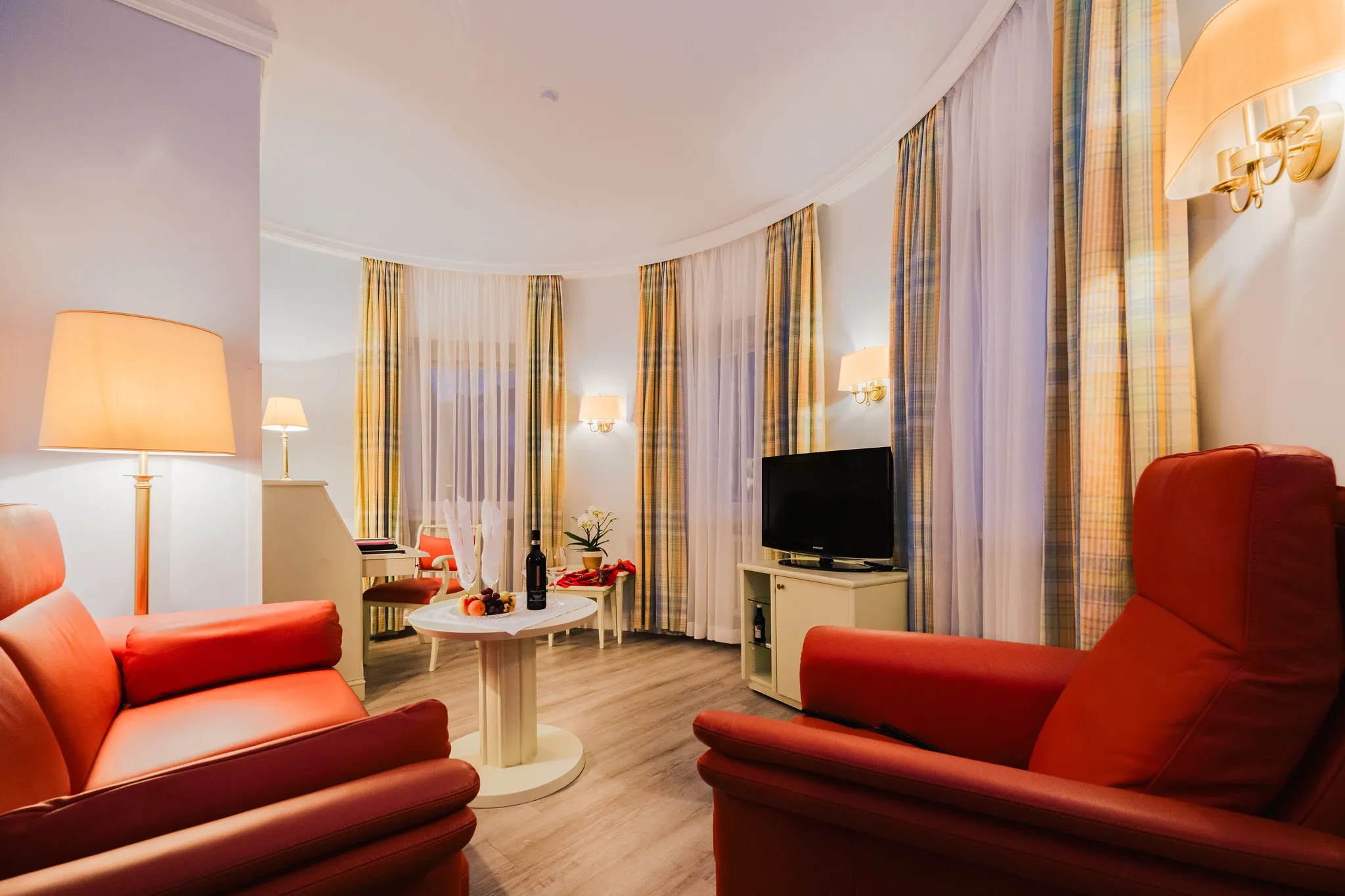 Hotel-Suite Wohnbereich mit roten Ledersesseln, Flachbildschirm und warmem Ambiente