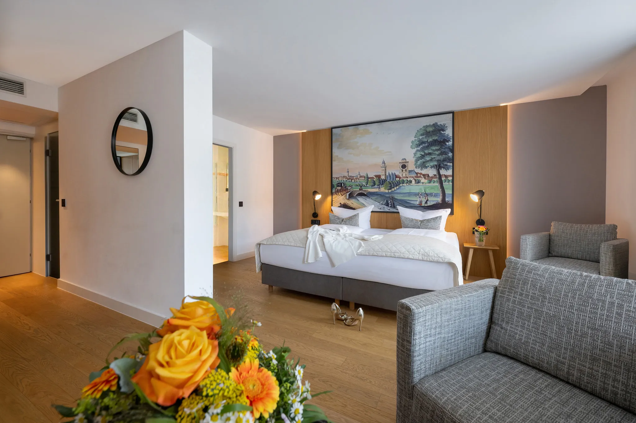 Helles Hotelzimmer mit historischem Panoramagemälde über dem Bett und frischen Rosen im Vordergrund