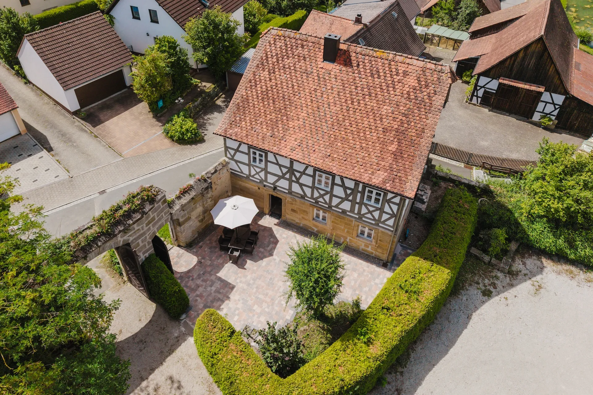 Luftaufnahme eines Fachwerkhauses mit gepflastertem Innenhof und Gartenterrasse aus der Vogelperspektive