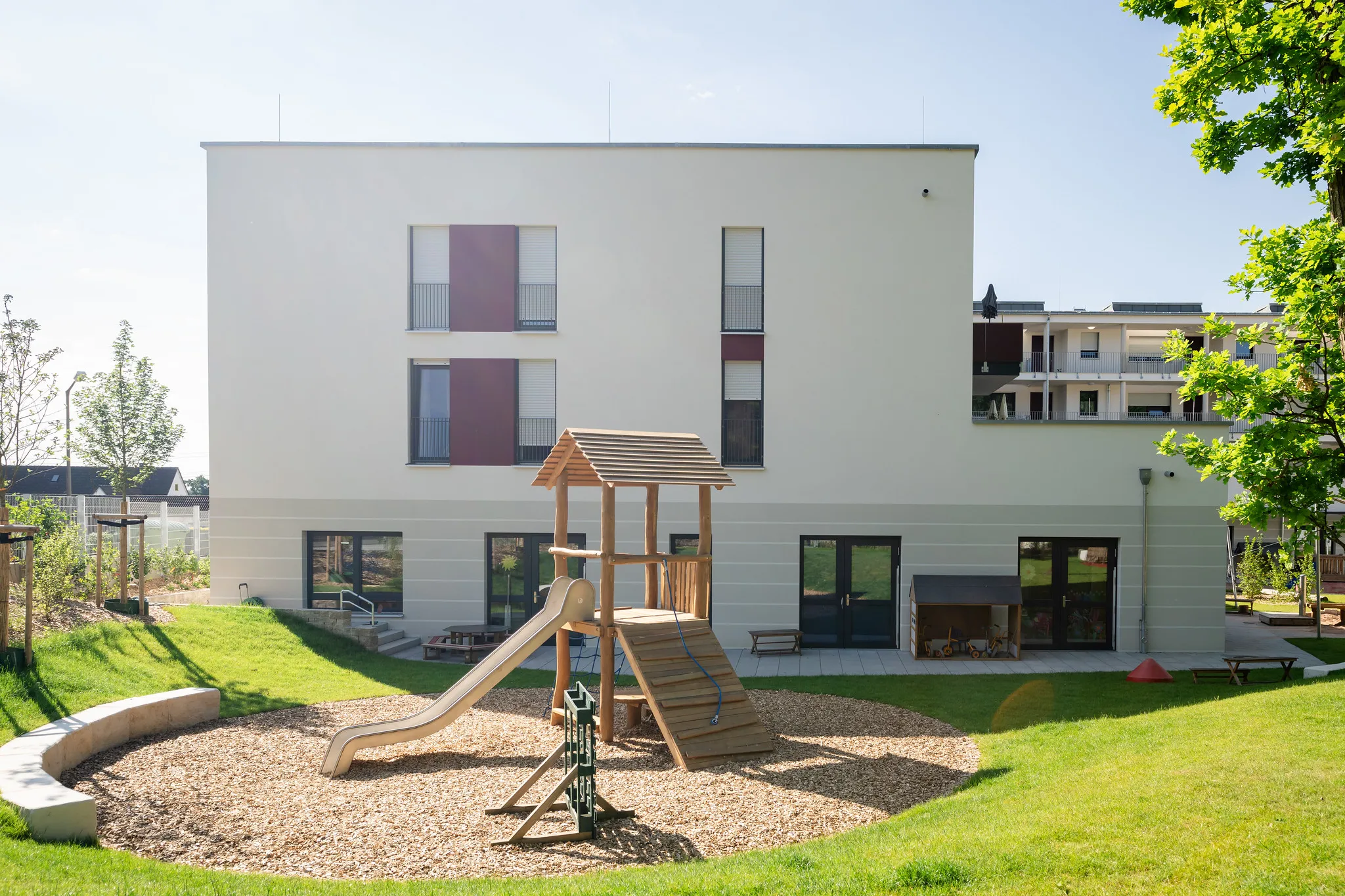 Kita-Gebäude mit Spielplatz und Rutsche im Garten.