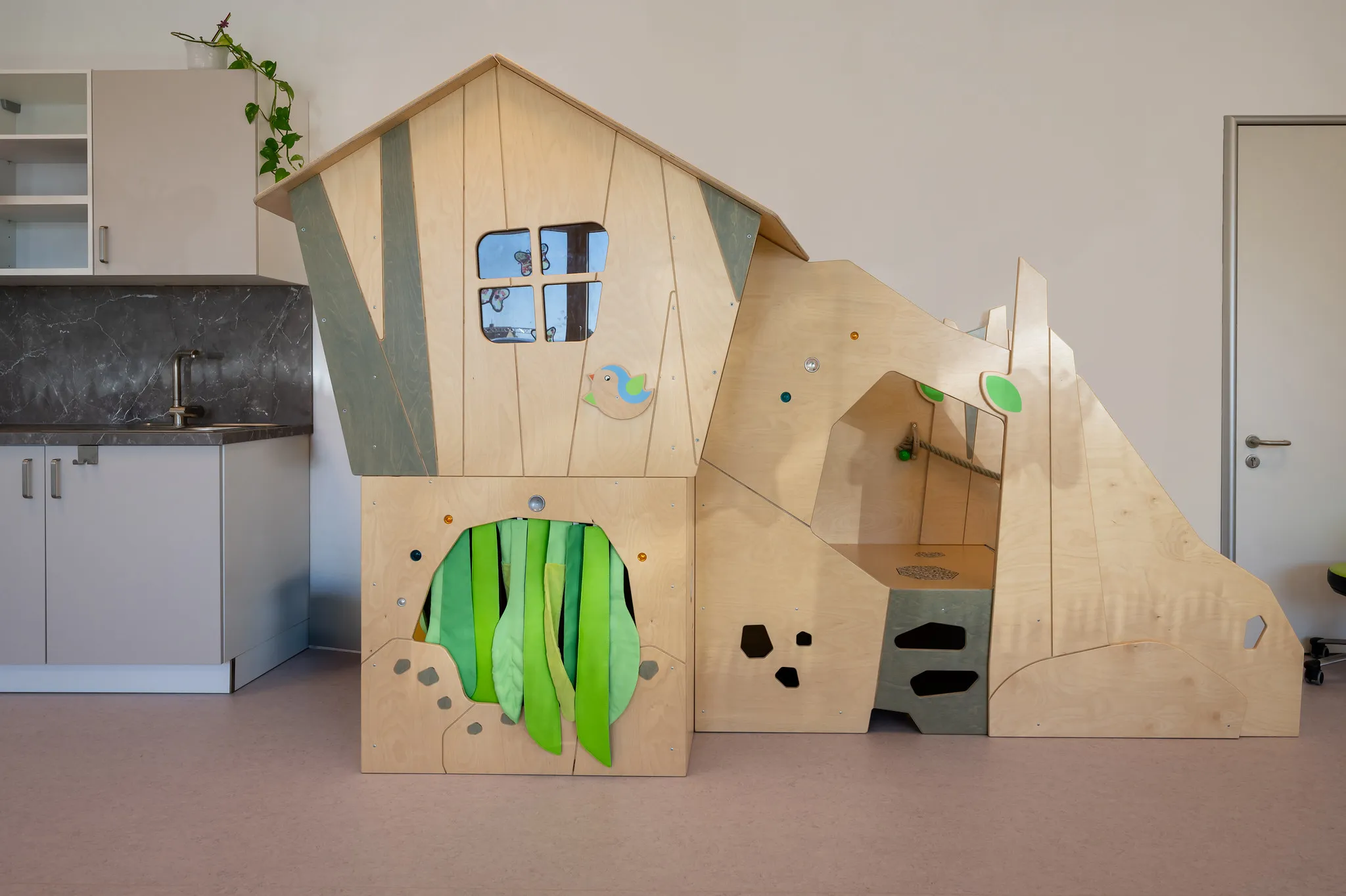 Kita-Innenraum mit Holz-Spielhaus und Rutsche.