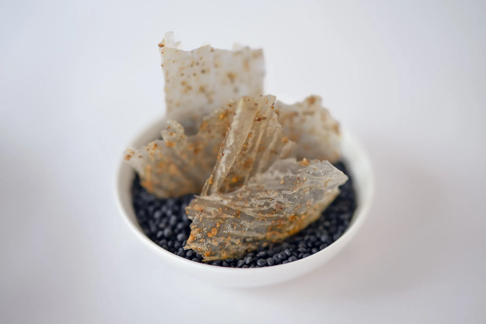Knusprige, hauchdünne Chips in weißer Schale auf schwarzen Belugalinsen, Detailaufnahme Fine Dining.