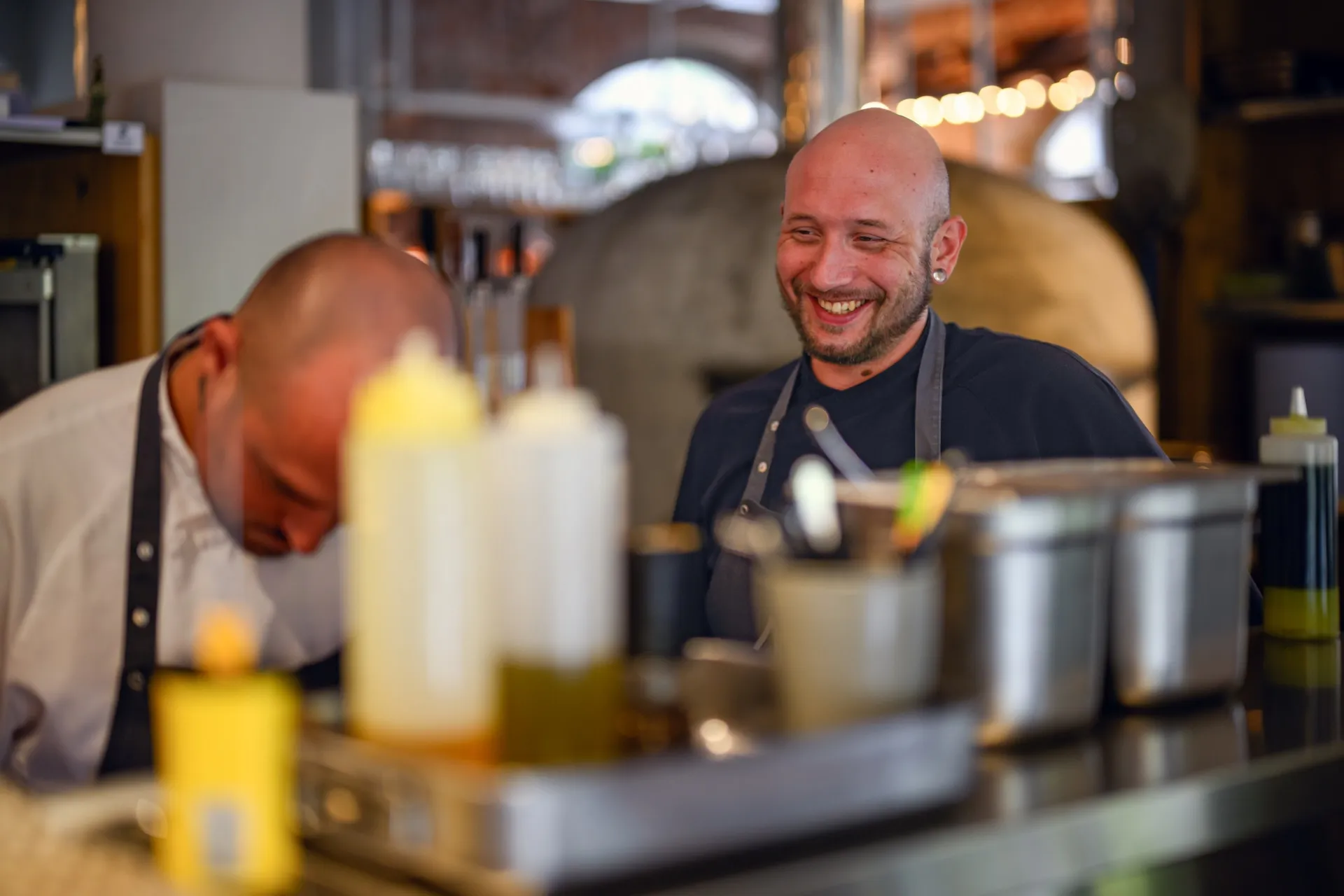 Köche lachen in offener Küche, authentische Gastro-Atmosphäre.