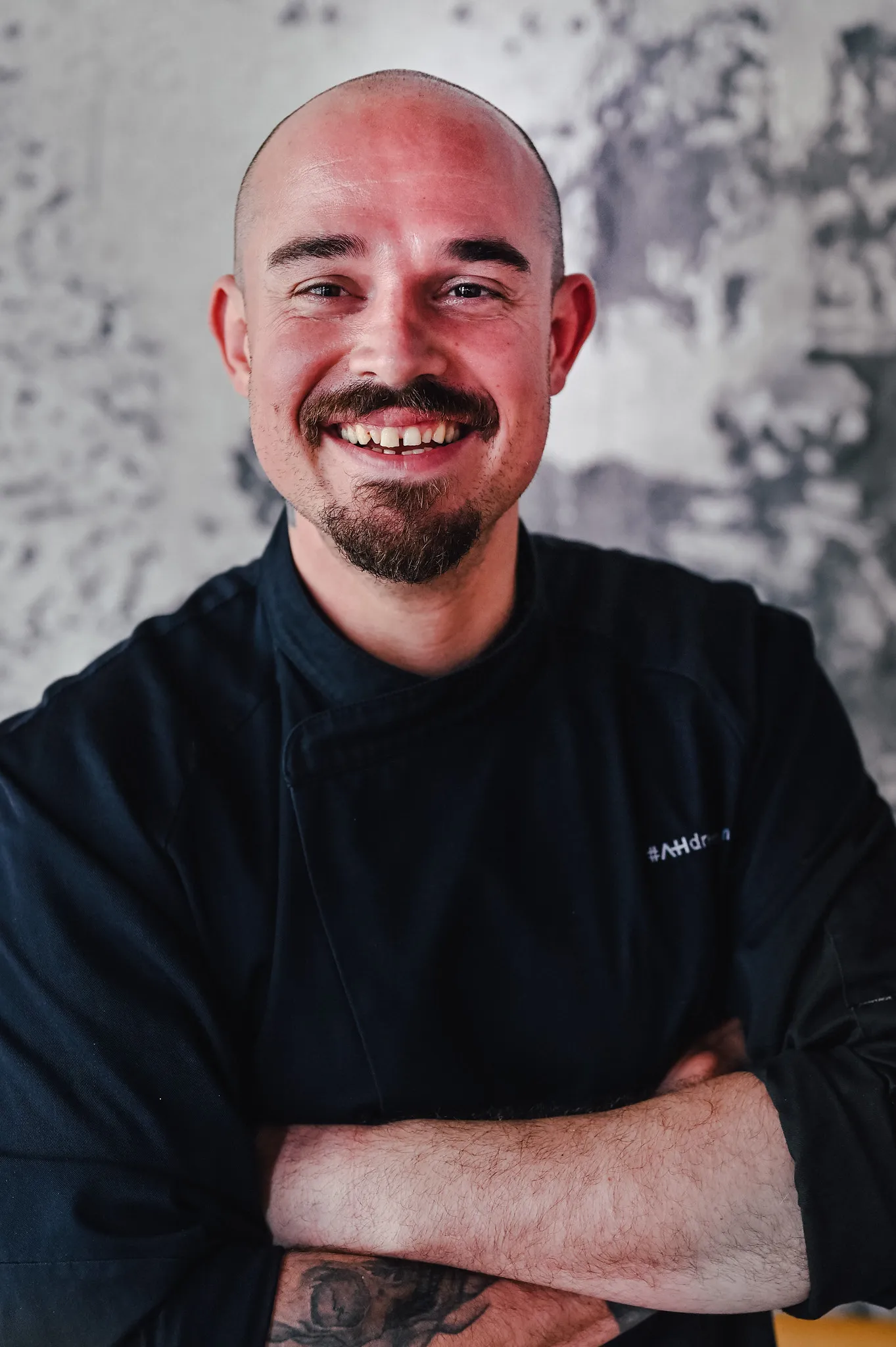 Lächelnder Mann mit Glatze und Goatee in schwarzer Kochjacke, Business-Portrait mit Charakter