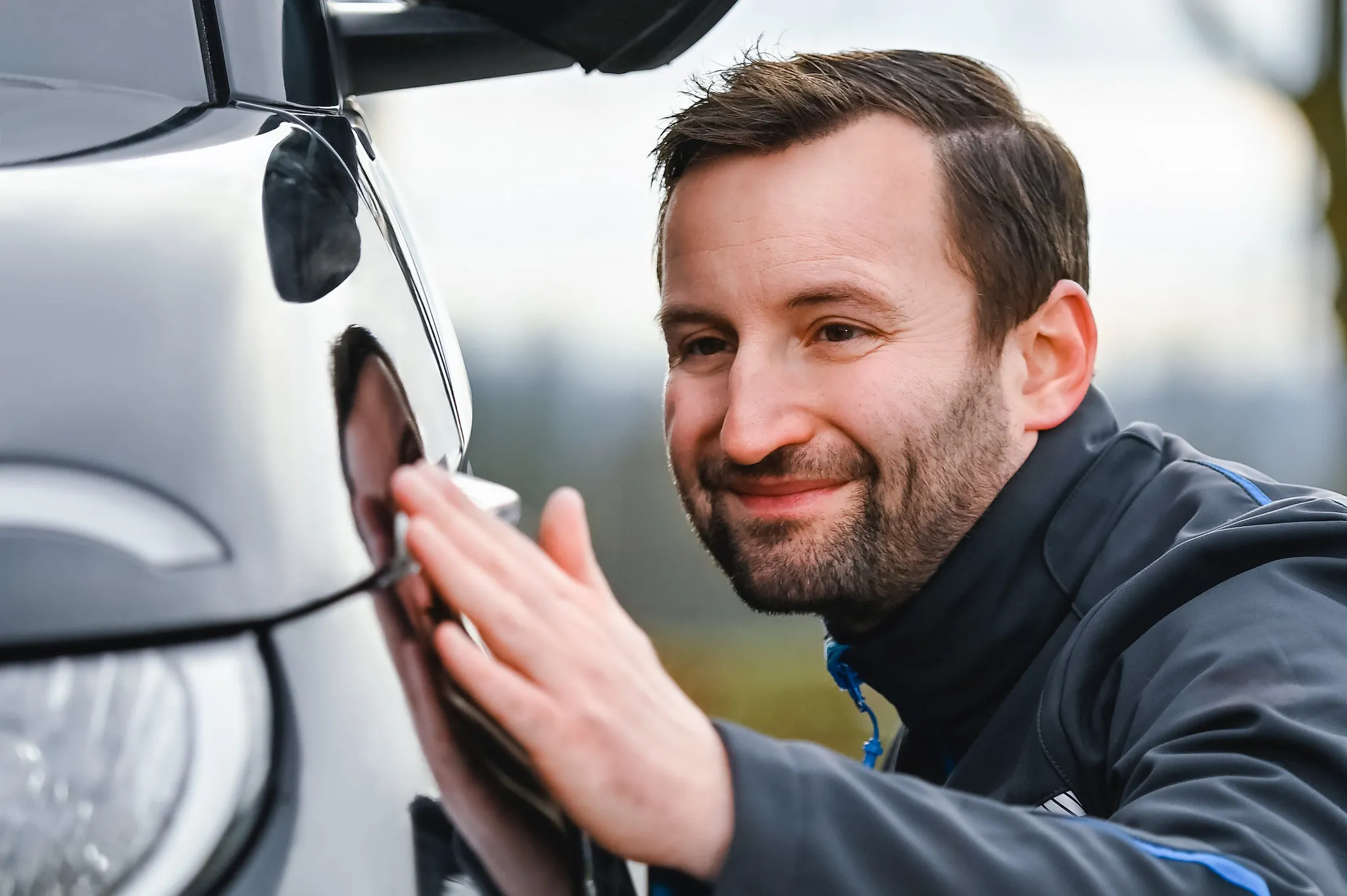 Lächelnder Mann in Nahaufnahme an einem Auto, natürliches Business-Portrait im Freien