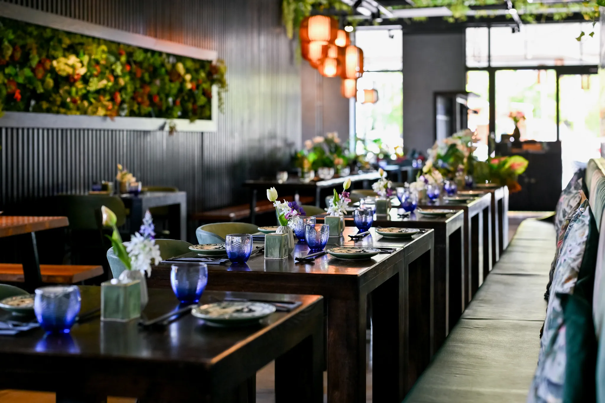 Lange eingedeckte Tafel mit blauen Gläsern, Blumenvasen und Pflanzenwand, Restaurantfotografie Nürnberg.