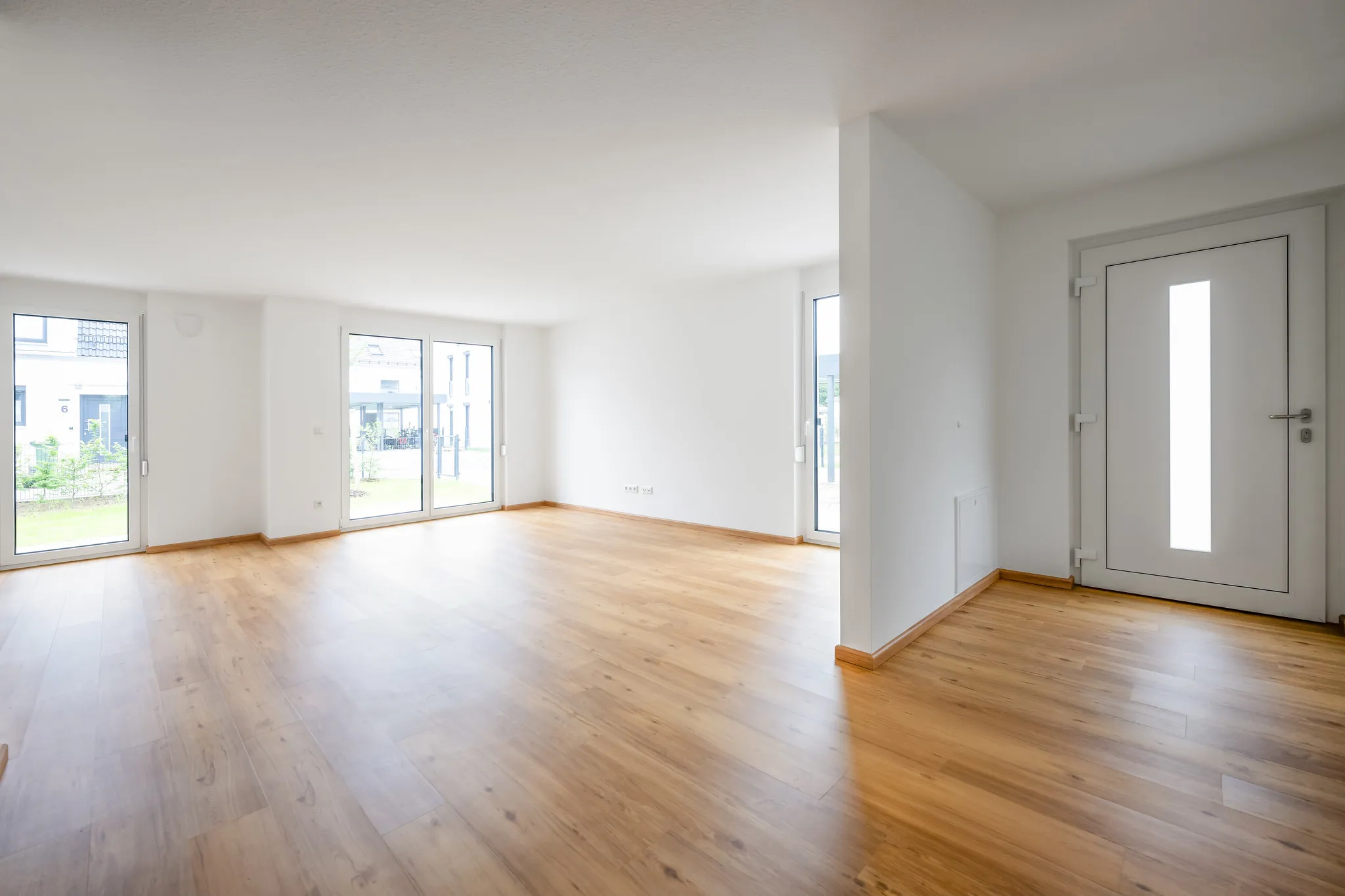 Leeres Wohnzimmer mit Parkett und bodentiefen Fenstern.