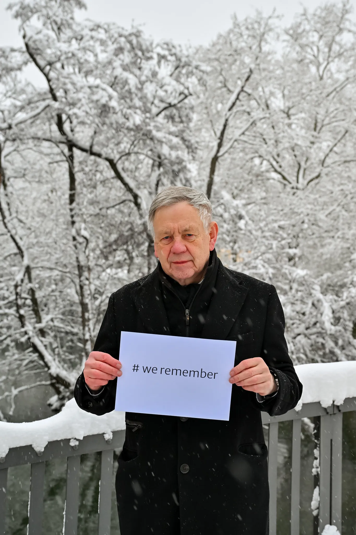 Mann hält We-Remember-Schild bei Gedenkveranstaltung im Winter