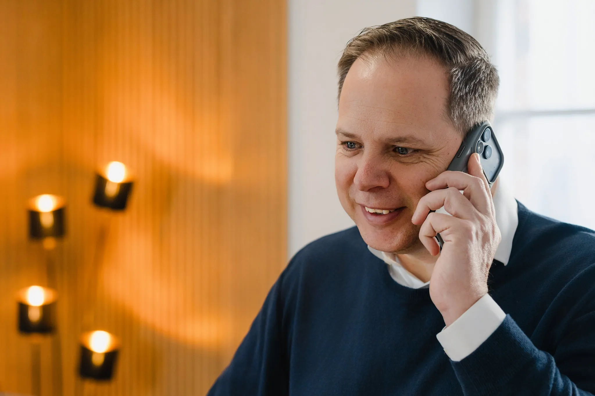 Mann im dunkelblauen Pullover telefoniert und lächelt, warmes Business-Portrait