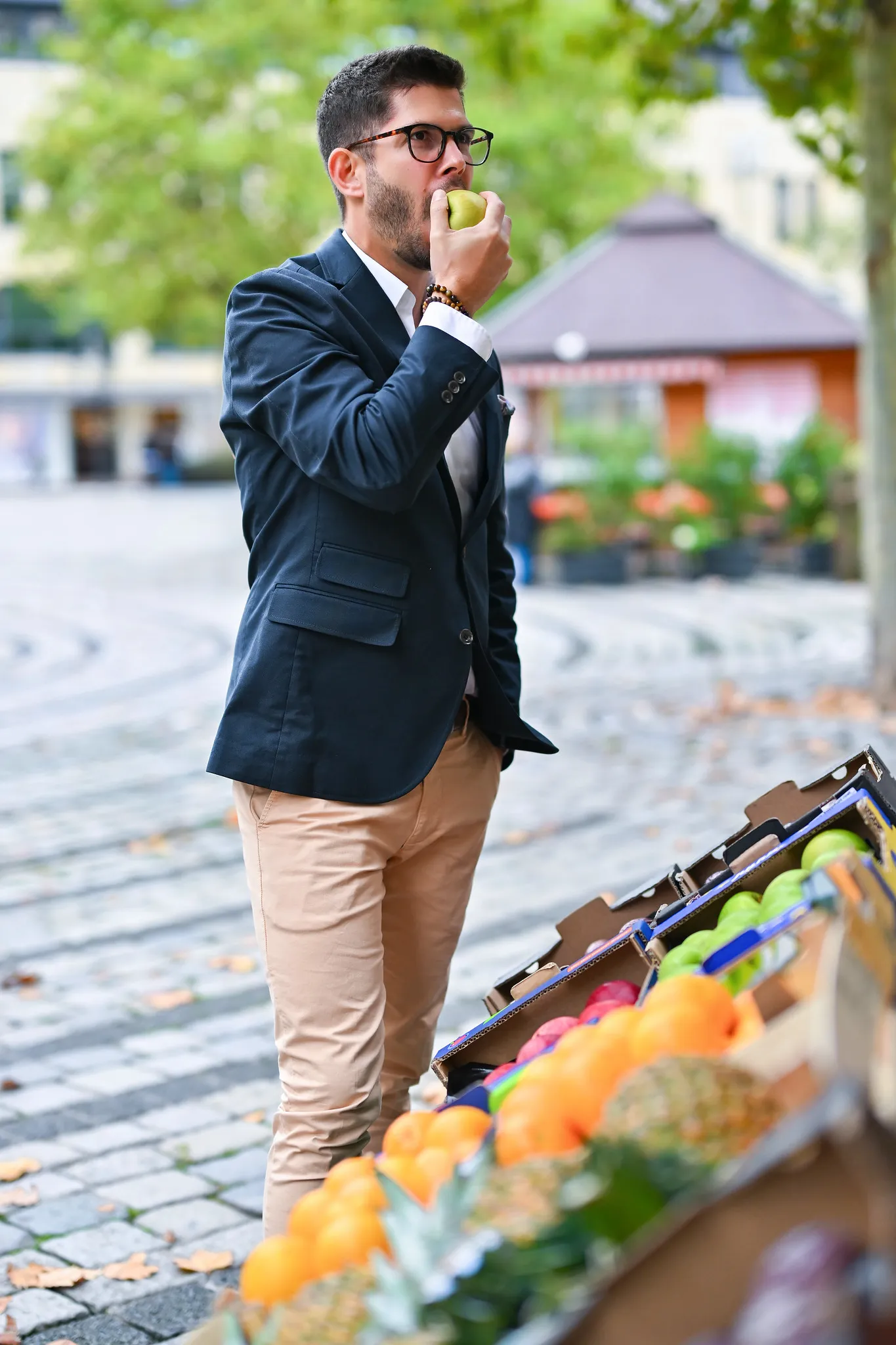 Mann im Sakko isst einen Apfel am Marktstand, lockeres Business-Portrait im Freien
