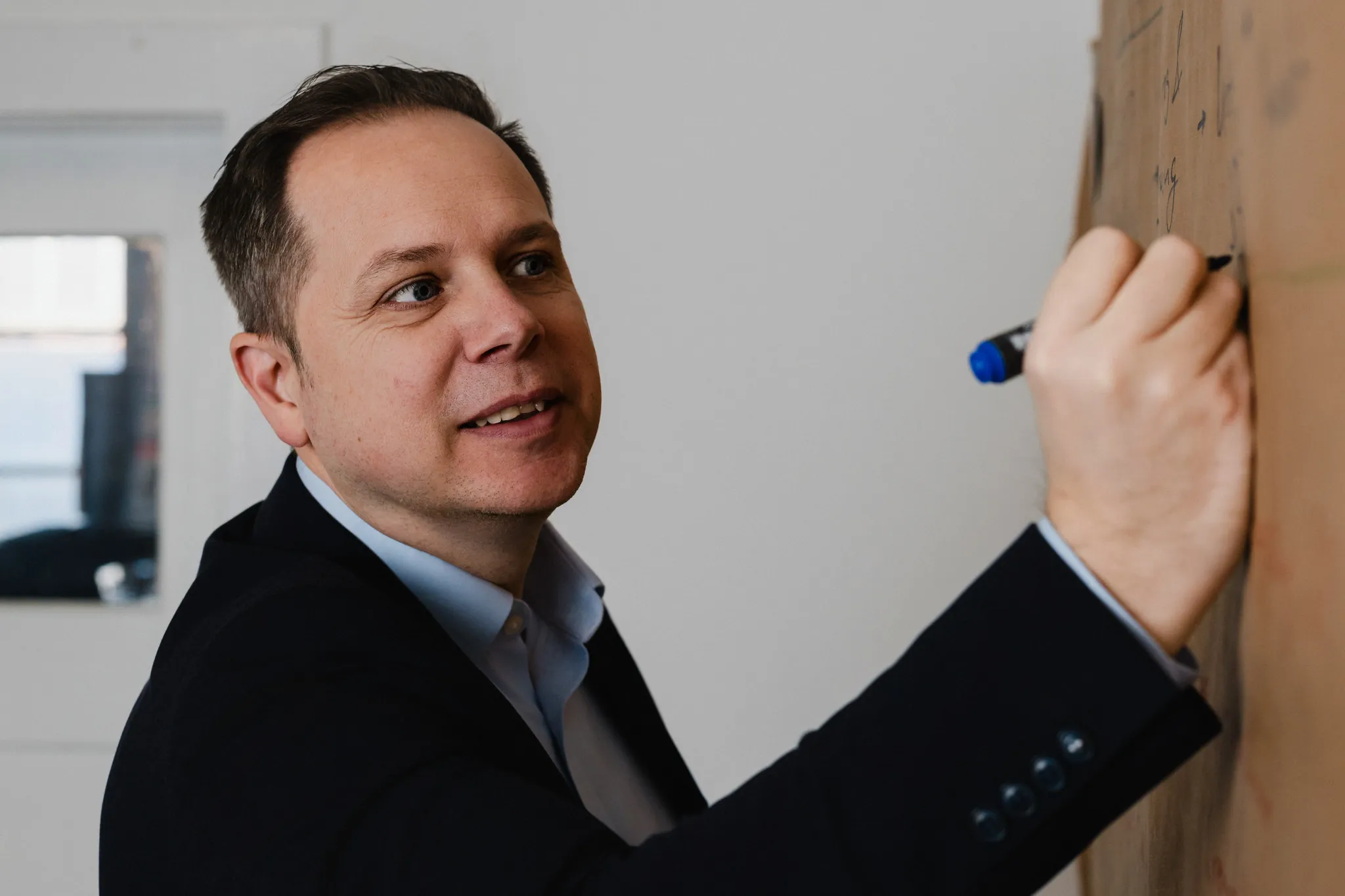 Mann im Sakko schreibt am Flipchart und blickt in die Kamera, Business-Portrait im Workshop