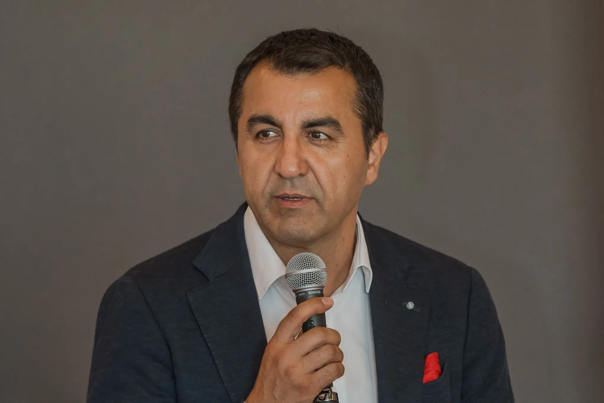 Mann im dunklen Sakko spricht ins Mikrofon, ausdrucksstarkes Business-Portrait beim Vortrag