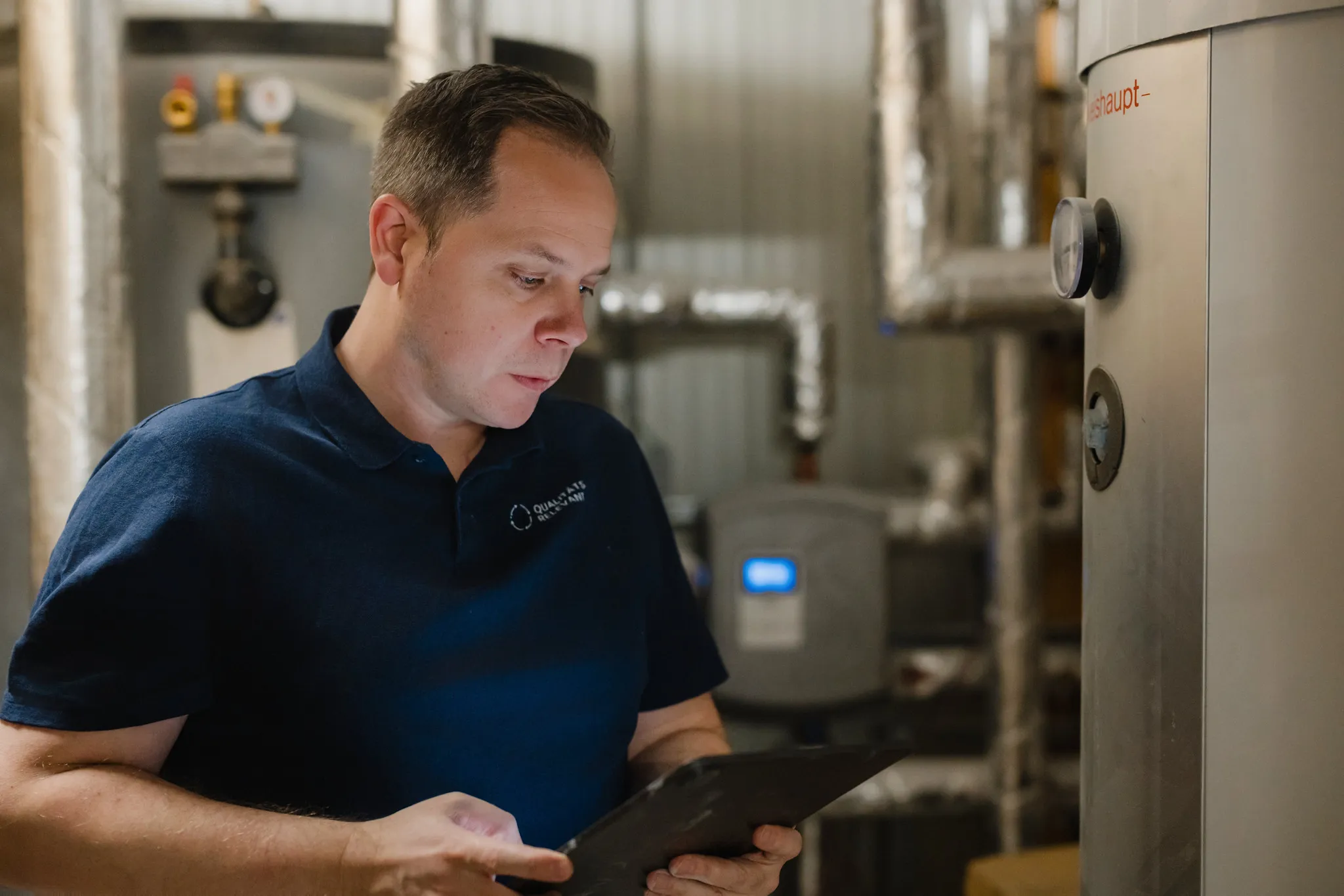 Mann im Poloshirt schaut im Technikraum auf ein Tablet, Business-Portrait am Arbeitsplatz