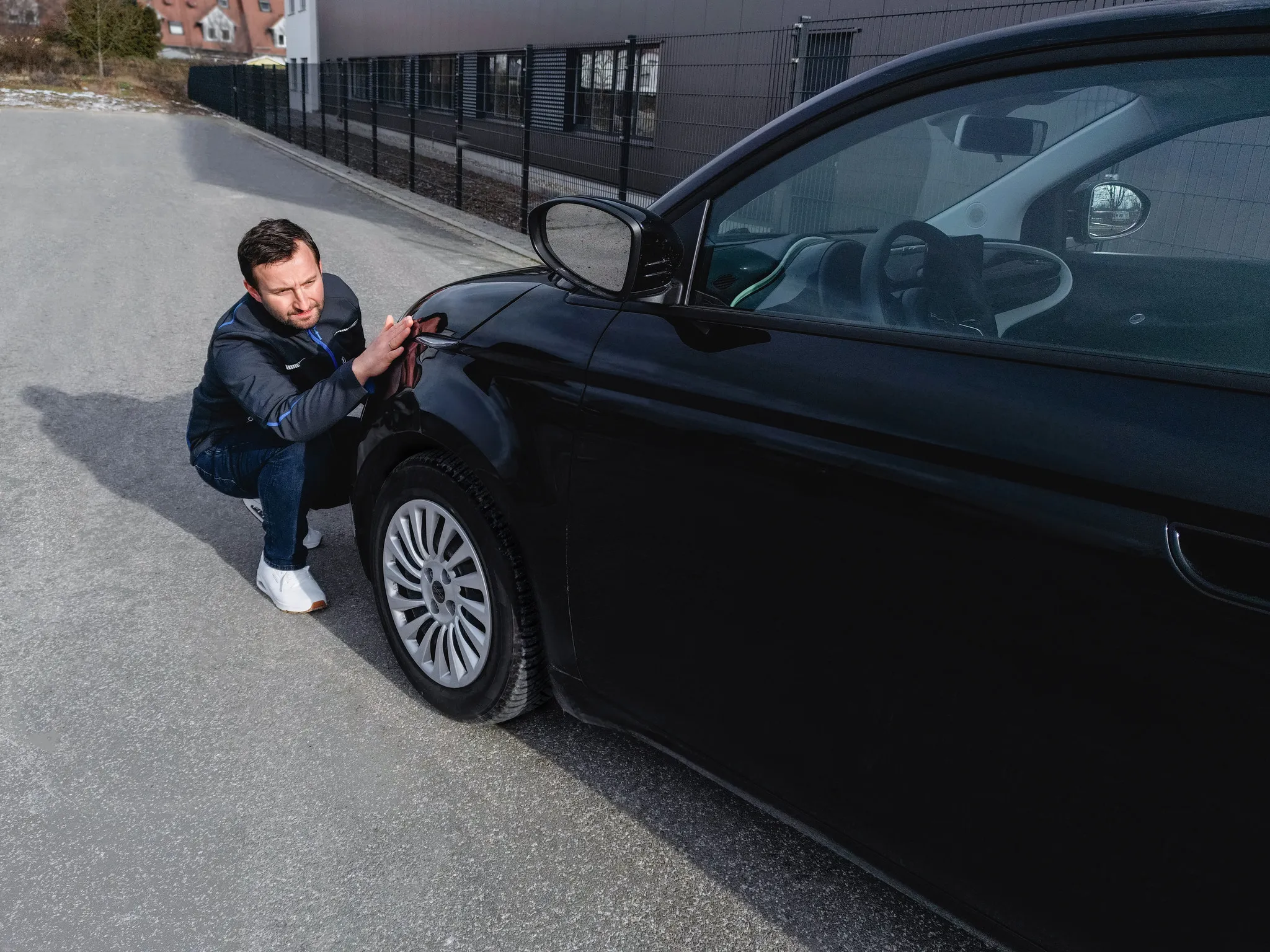 Mann kniet neben einem schwarzen Auto und prüft den Lack, Business-Portrait im Arbeitsumfeld