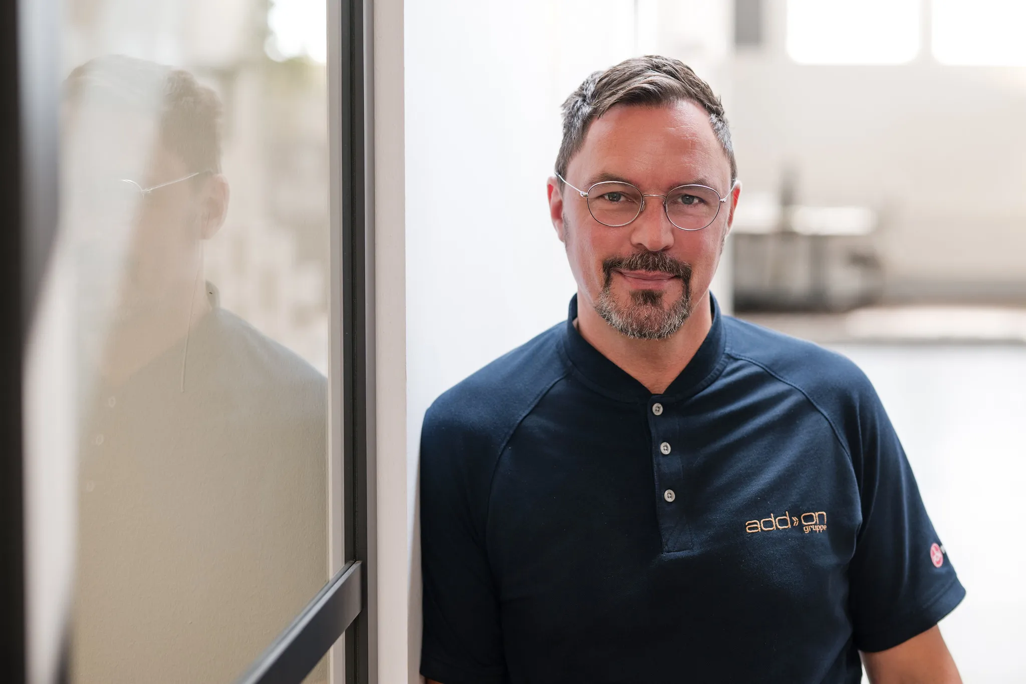 Mann mit Brille und dunklem Poloshirt lehnt am Fenster, ruhiges Business-Portrait