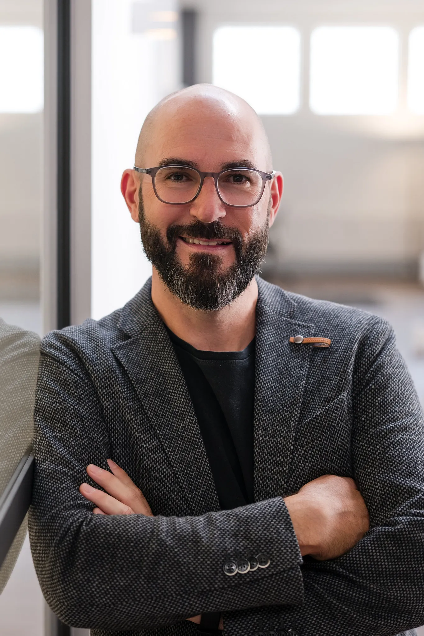 Mann mit Glatze, Bart und Brille im grauen Sakko, selbstbewusstes Business-Portrait mit verschränkten Armen