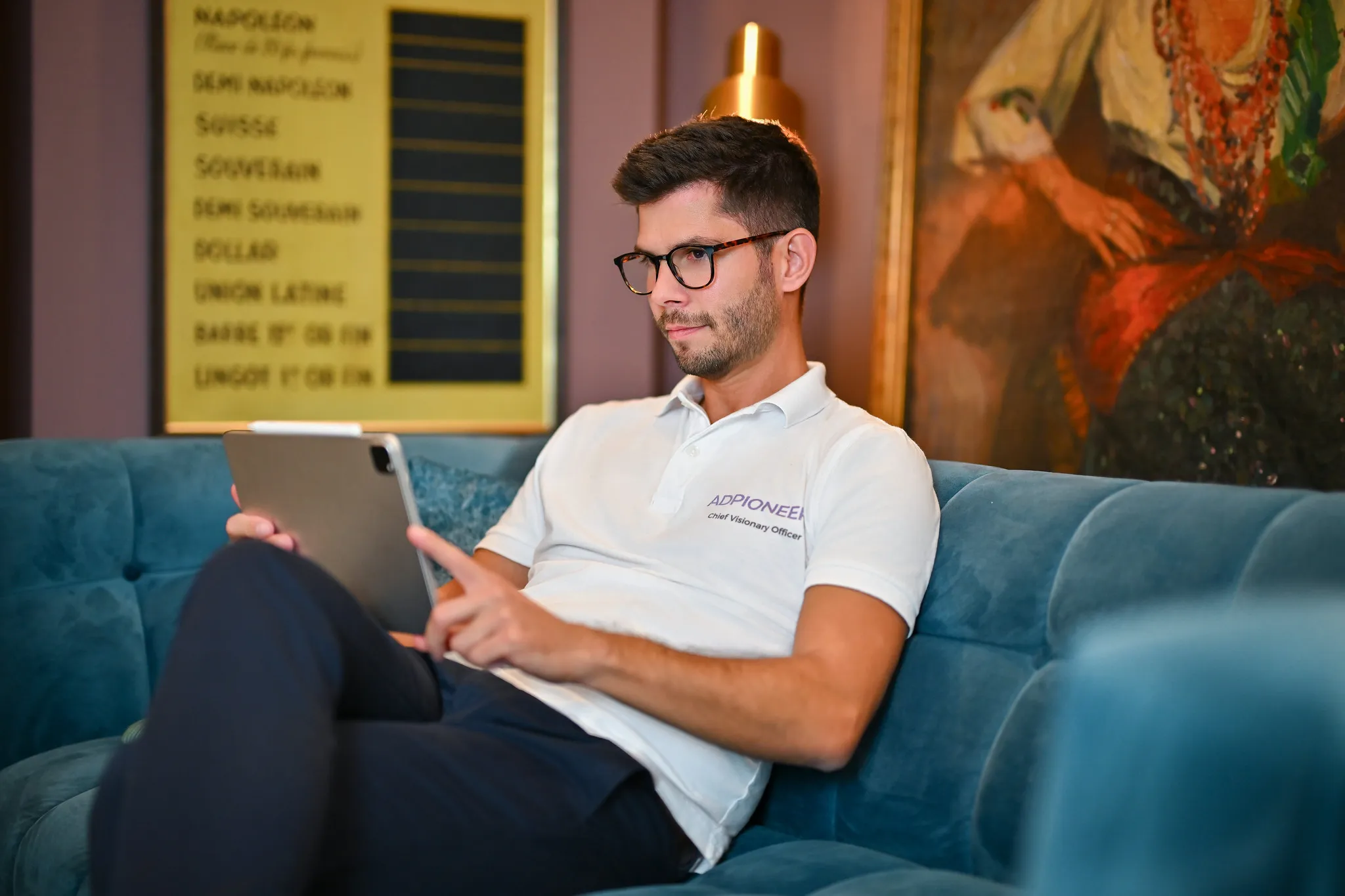 Mann im weißen Poloshirt mit Tablet auf blauem Sofa, entspanntes Business-Portrait