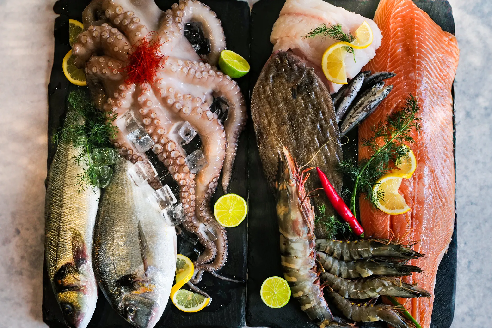 Meeresfrüchteplatte auf Schiefer mit Oktopus, Lachs, Garnelen und Zitrone.