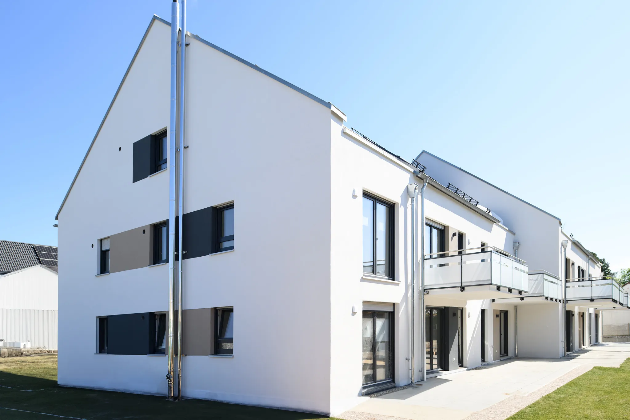 Weißes Mehrfamilienhaus mit Satteldach, Außenansicht im Sonnenlicht.