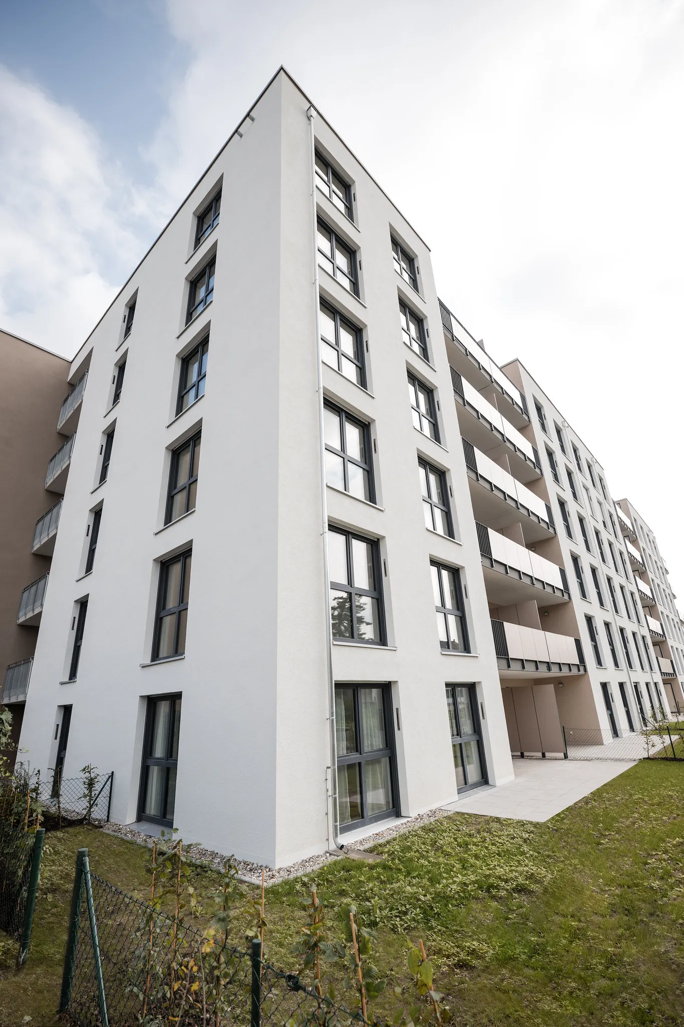 Eckansicht moderner Wohngebäude mit weißer Fassade und Balkonen.