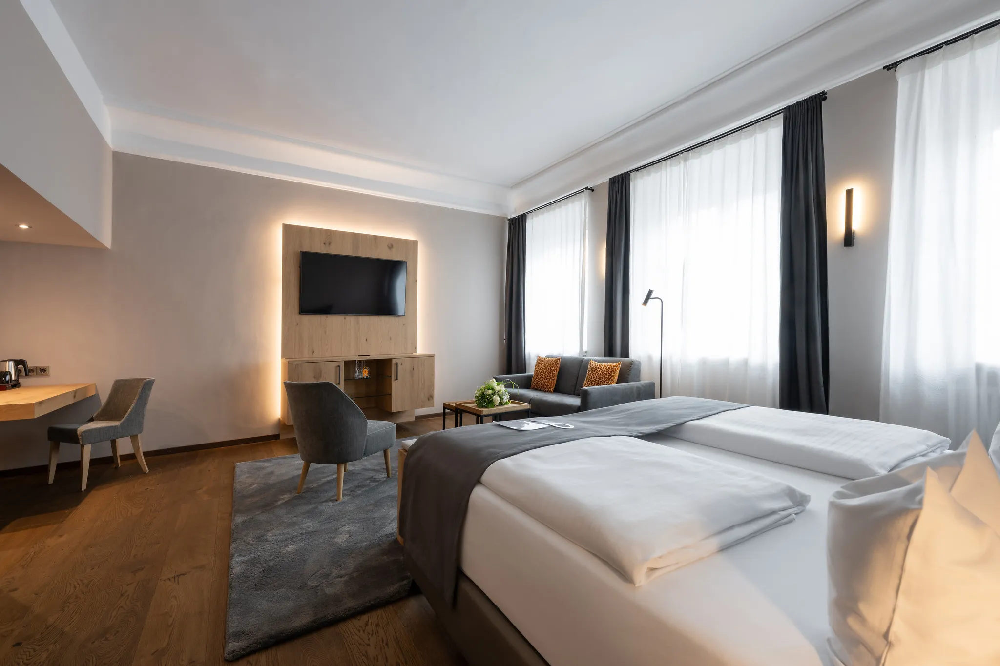 Modernes Hotelzimmer mit TV-Wandpaneel, gemütlicher Sitzecke und Doppelbett