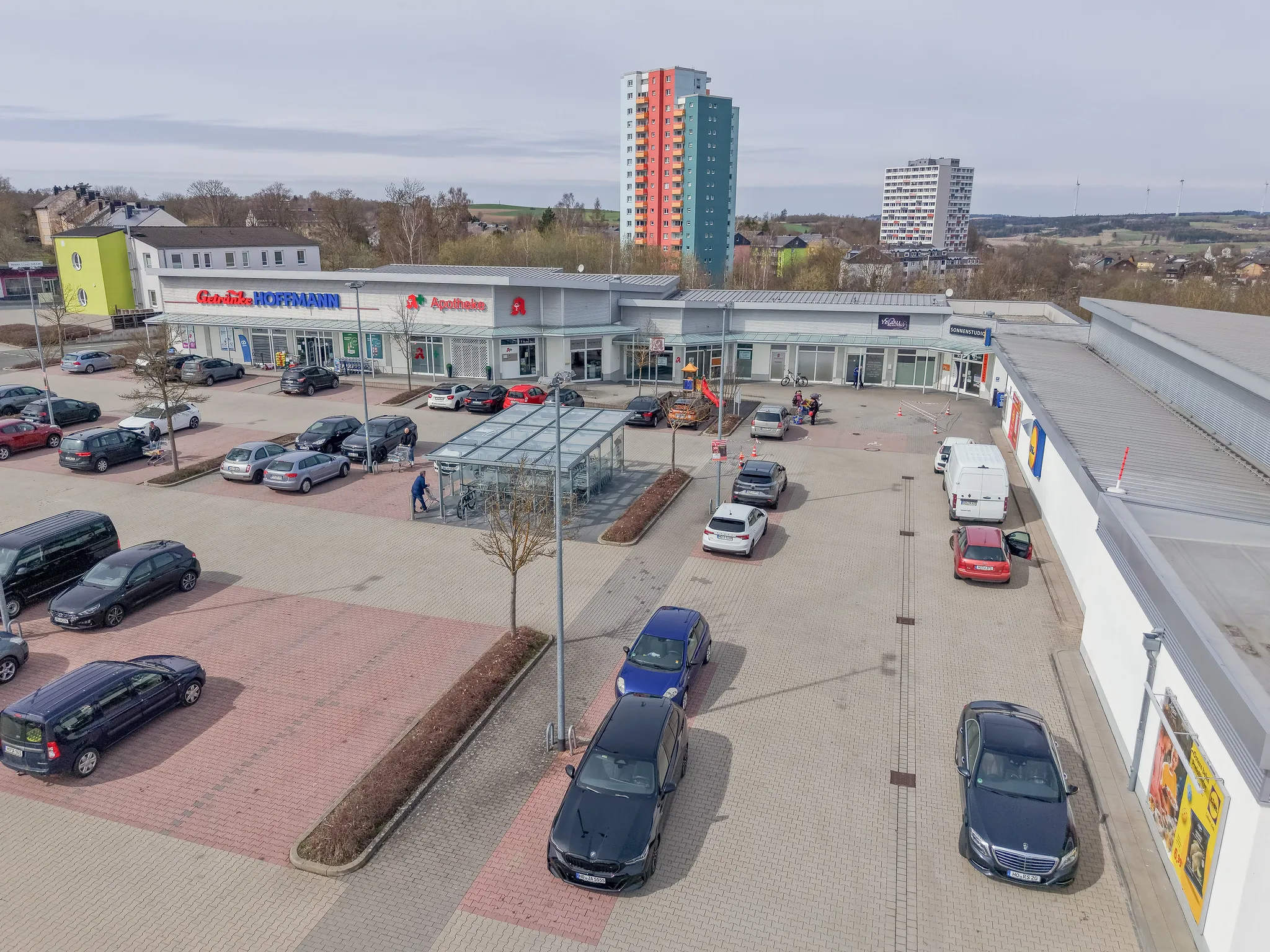Luftaufnahme eines Nahversorgungszentrums mit Getränkemarkt, Apotheke und Parkplatz