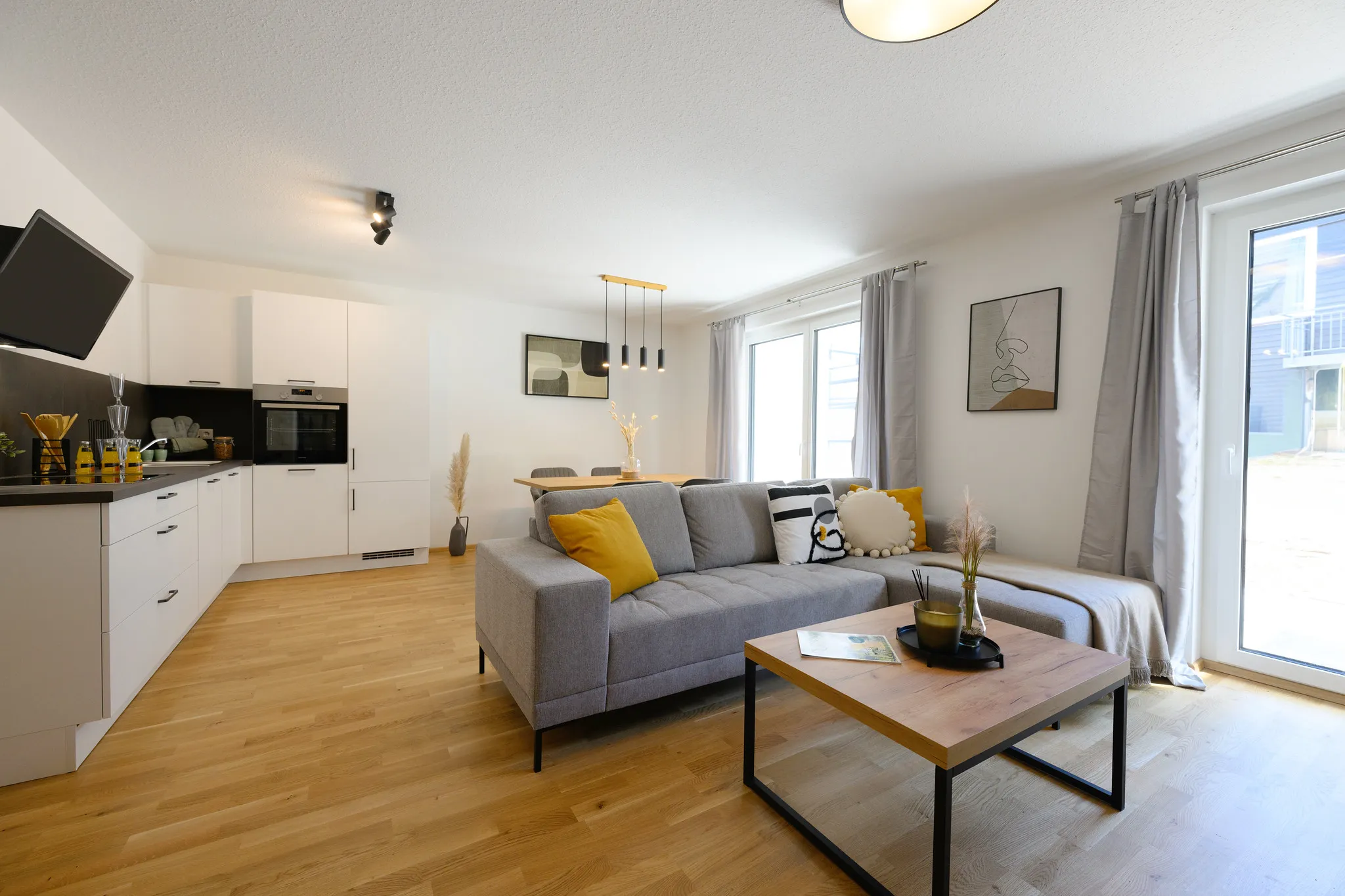 Offener Wohnbereich mit Küchenzeile und grauem Sofa.